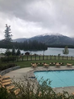 Outdoor swimming pool with turquoise water nestled against a forested mountainside under cloudy skies