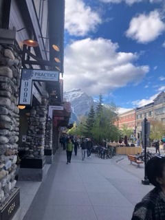 Pedestrians walking on a downtown street with historic stone buildings and a mountain peak visible in the distance
