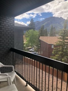 Mountain valley view from a residential balcony with forested slopes and peaks framed by the railing