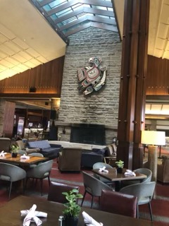 Modern hotel lobby with high ceilings, stone fireplace, and contemporary furnishings overlooking mountain scenery