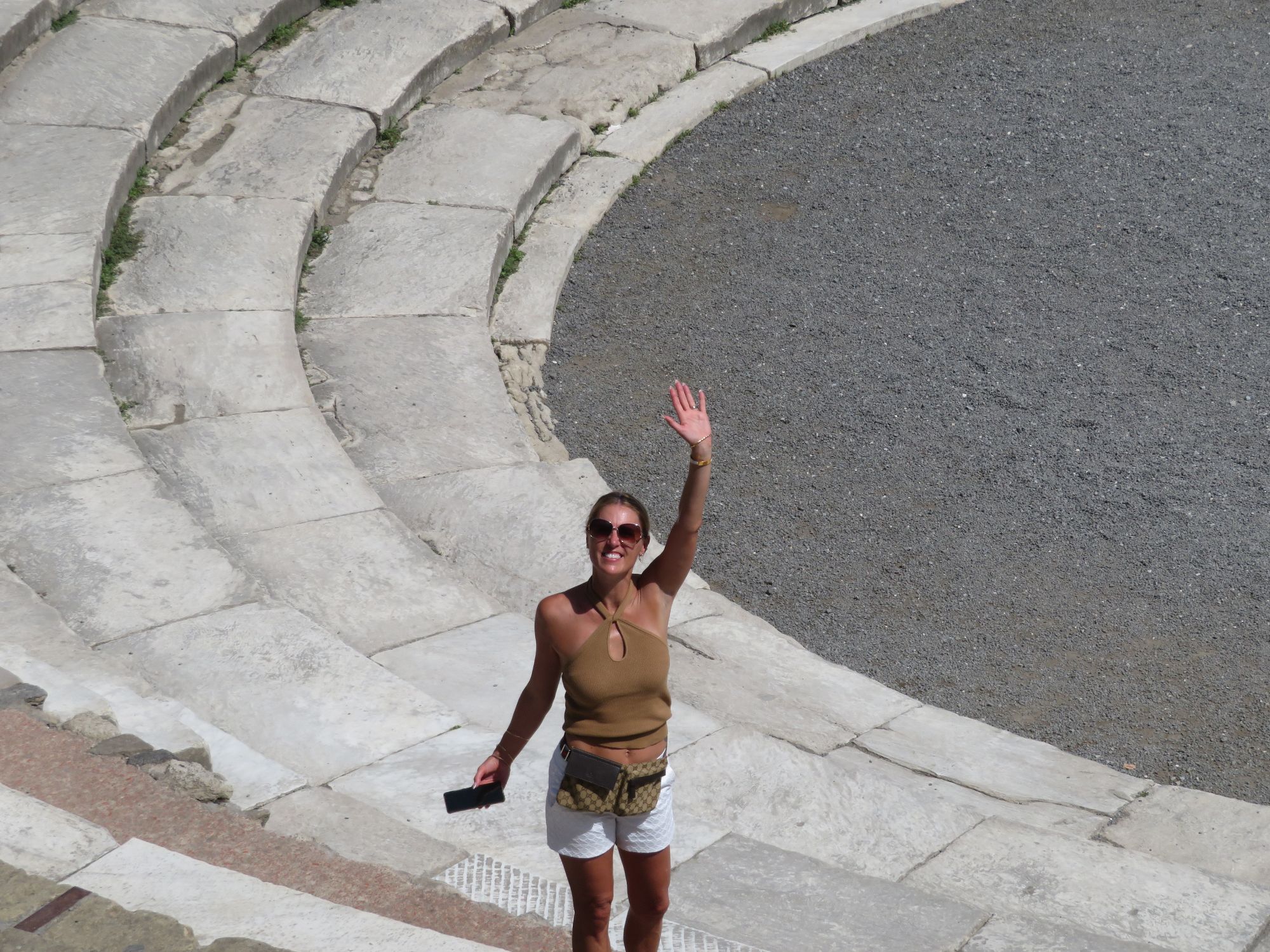 Maria Stainburn stands on curved concrete sea defense blocks, waving at the camera on a sunny day