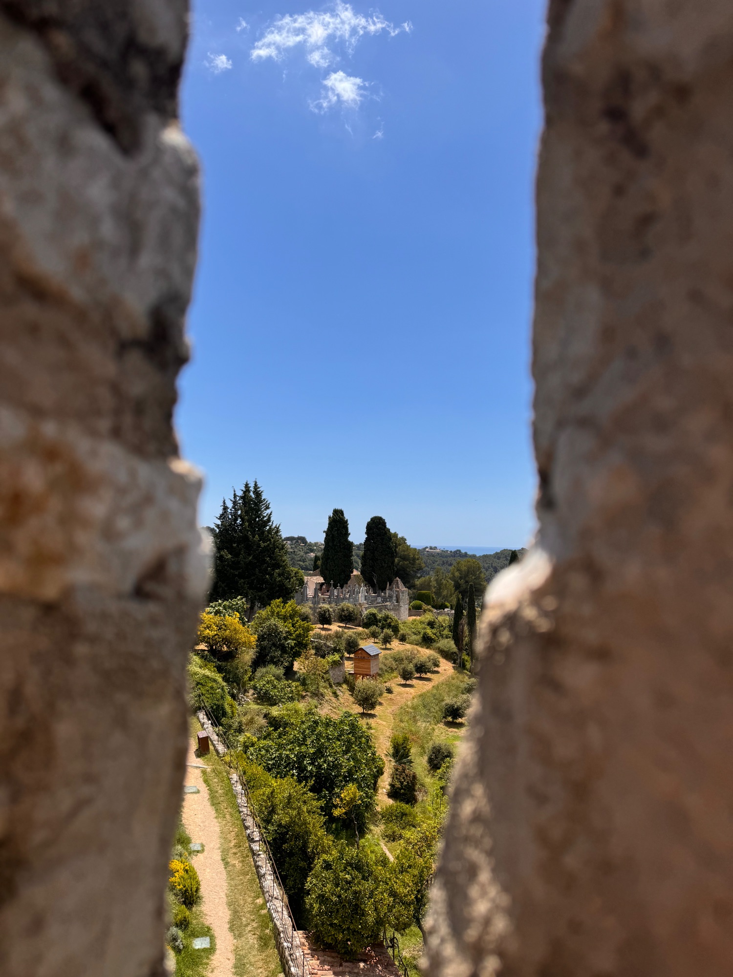 View through stone archway of lush green valley with cypress trees and distant hilltop buildings in Provence
