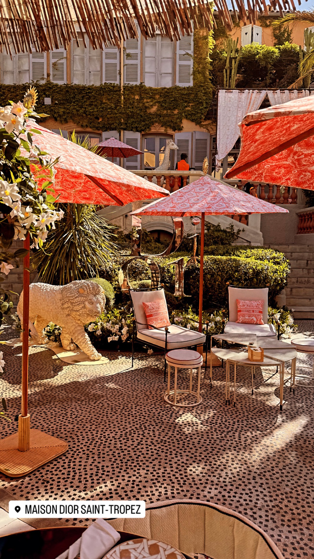 Luxury hotel courtyard with red patterned umbrellas, lounge chairs, and ivy-covered walls in Saint-Tropez