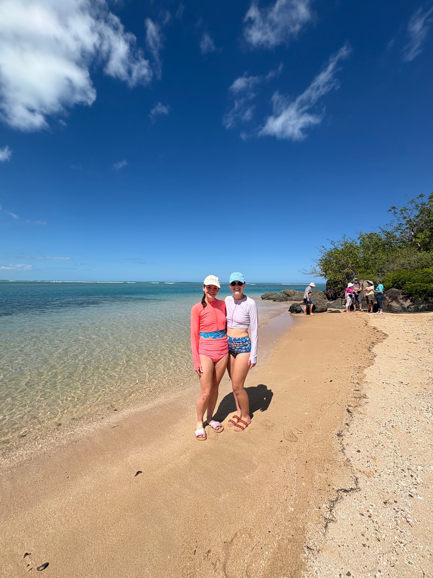 Two women in rash guards standing on sandy Puerto Rico beach with rocky outcrops behind
