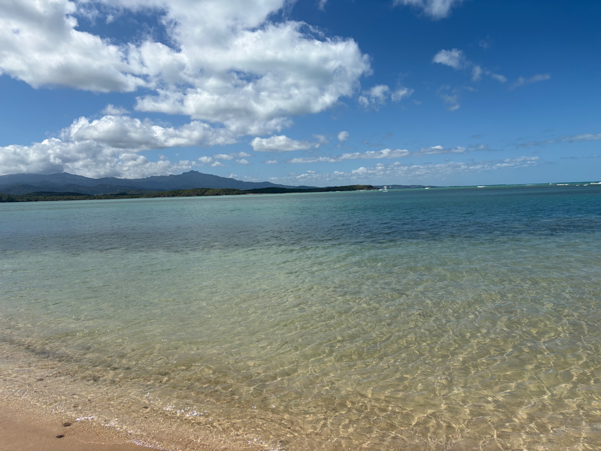 Calm turquoise lagoon with mountains across the water under partly cloudy sky