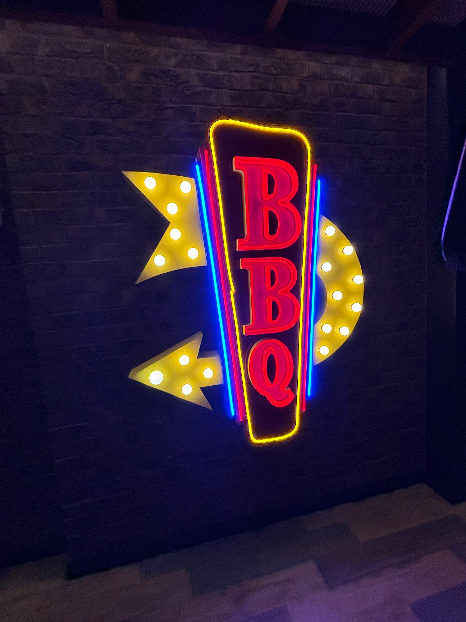 Neon sign reading BBQ with yellow lightning bolt arrows on dark brick wall