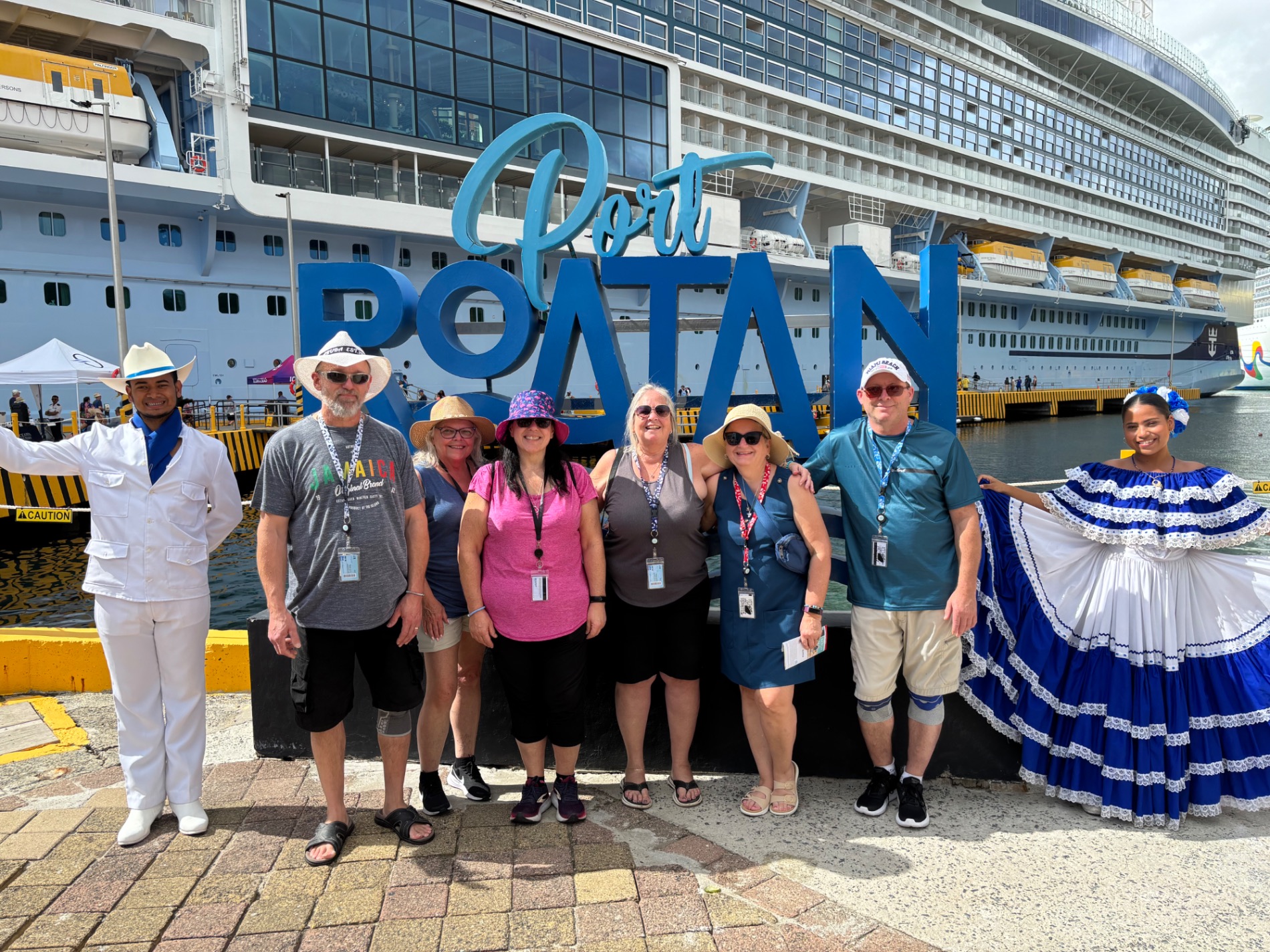 Group of eight people in casual cruise attire pose together in front of large blue Pool Boatain sign with cruise ship behind
