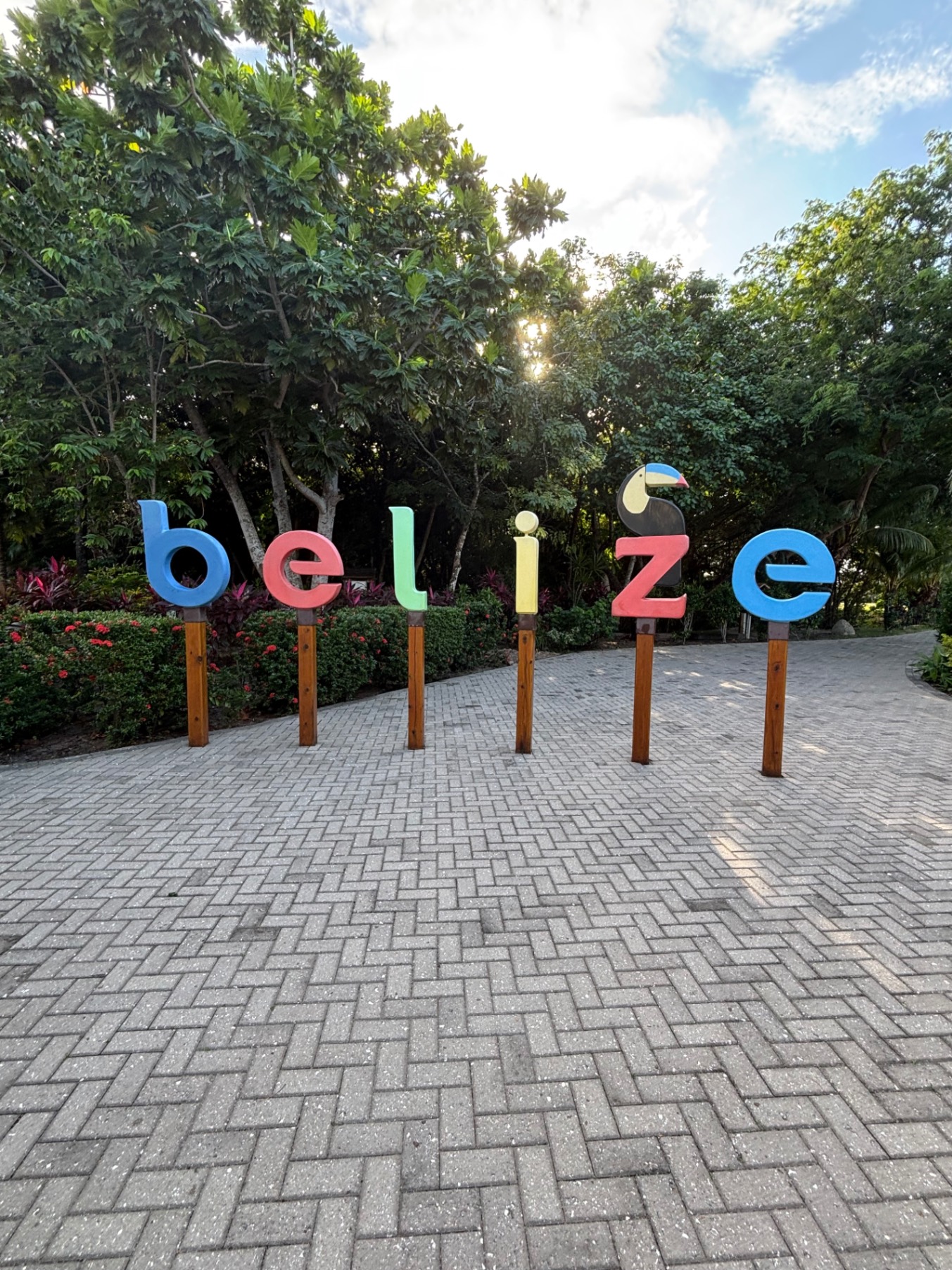Colorful letters spelling Belize stand on brick pathway surrounded by tropical trees and vegetation