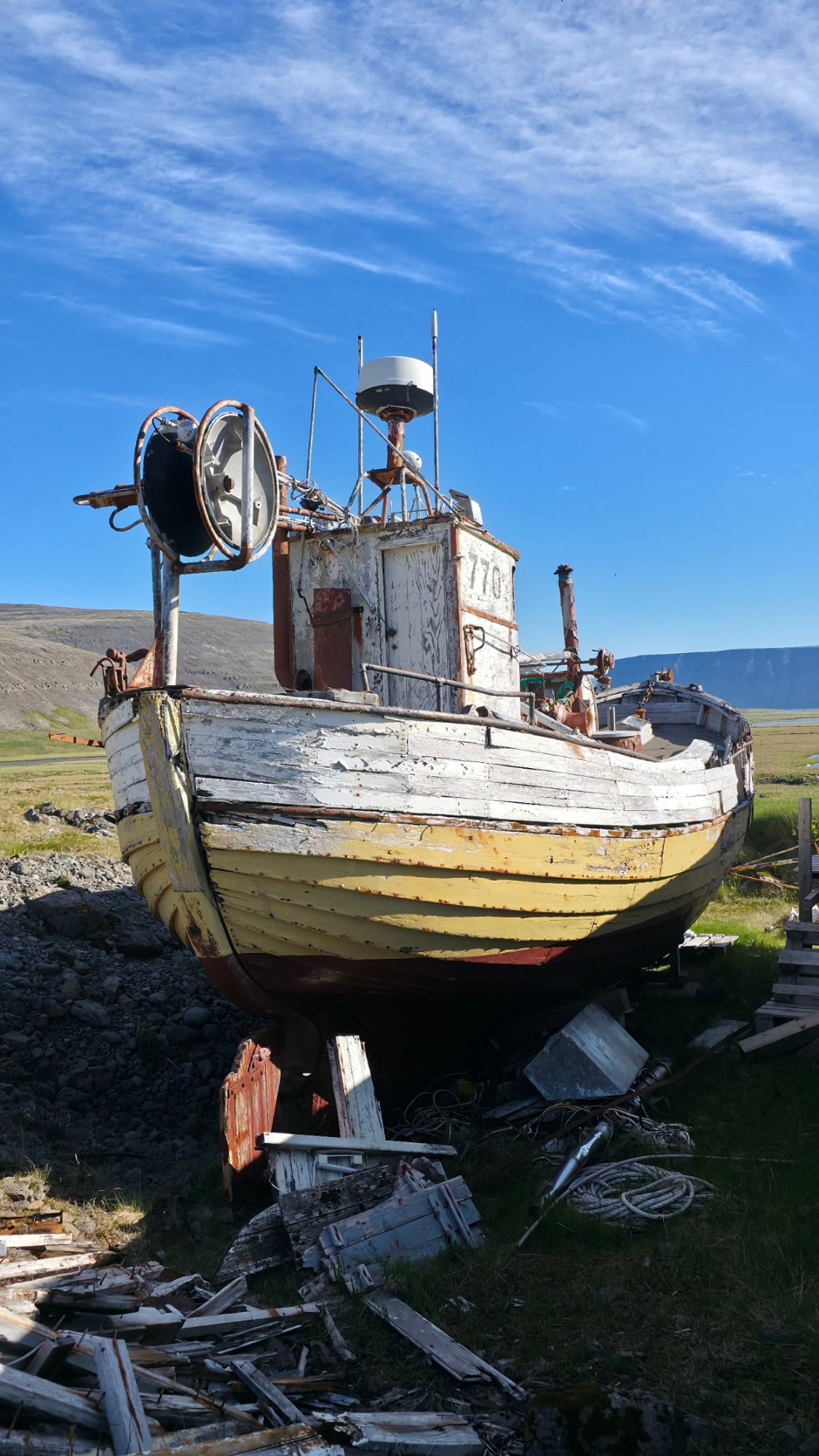 Abandoned fishing vessel with weathered white and yellow hull on grassy Icelandic landscape