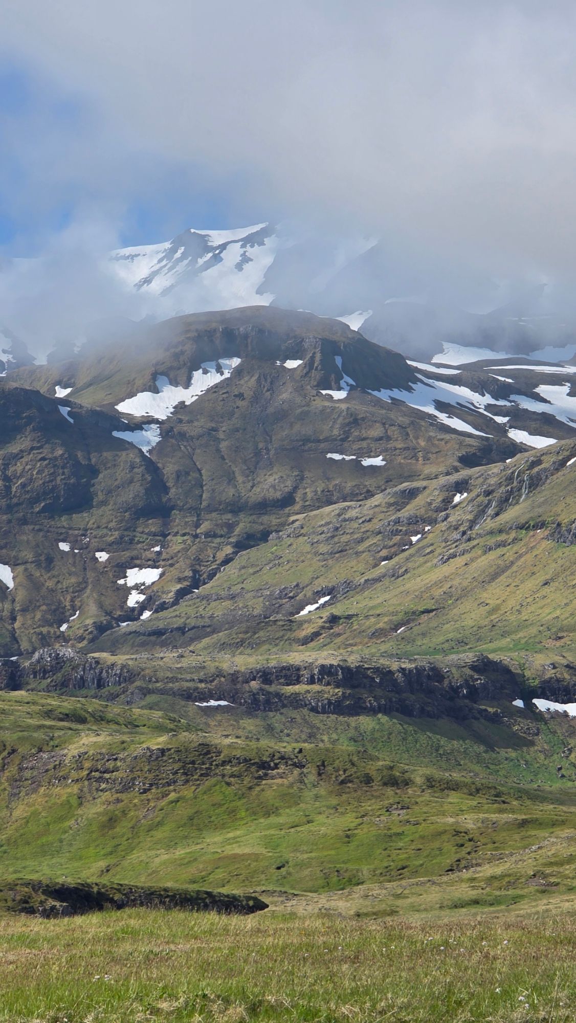Red farmhouse on fjord shore with mountains and waterfall in background, Iceland