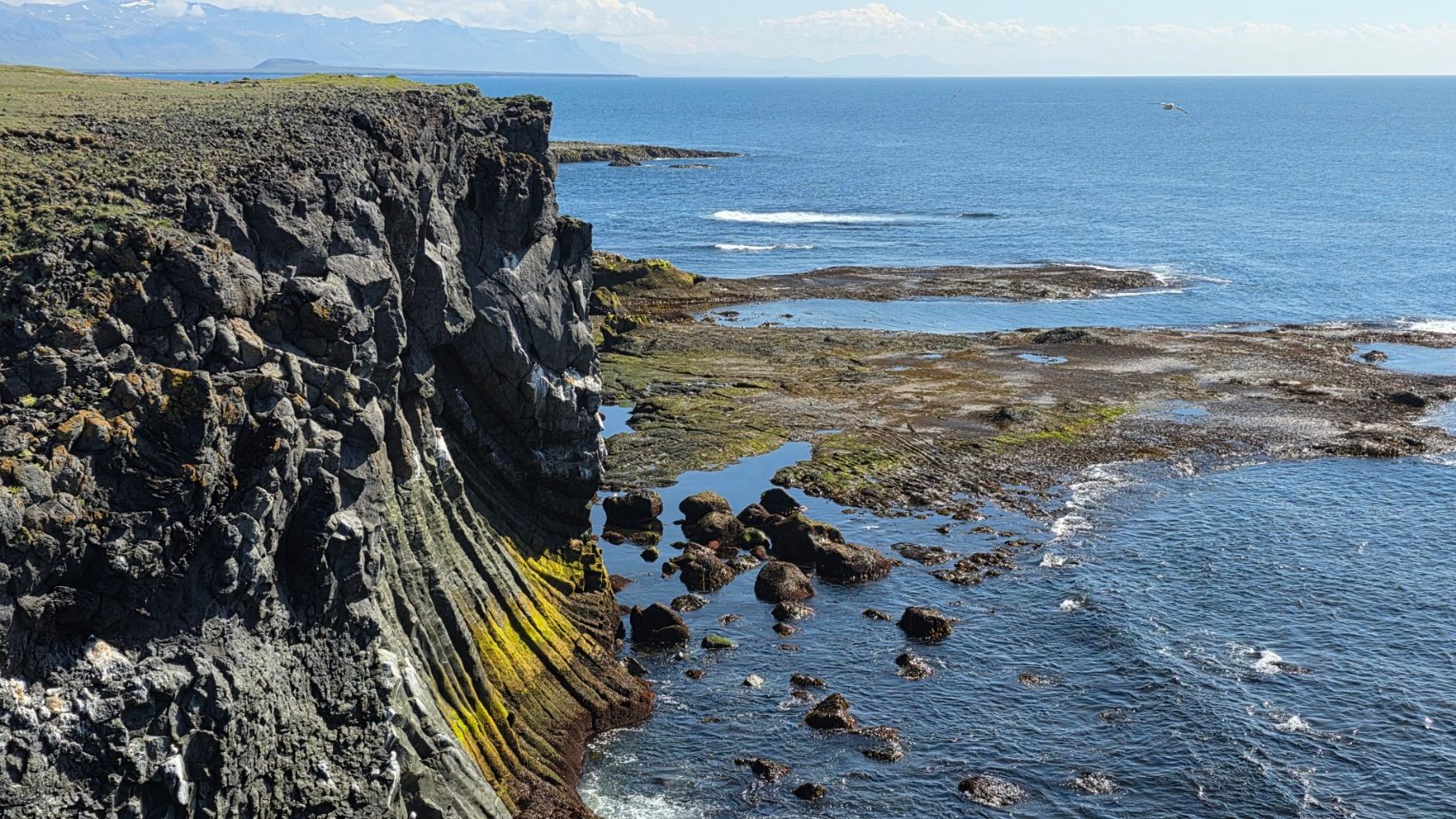 Abandoned fishing boat on rocky shore with mountains and waterfall in distance