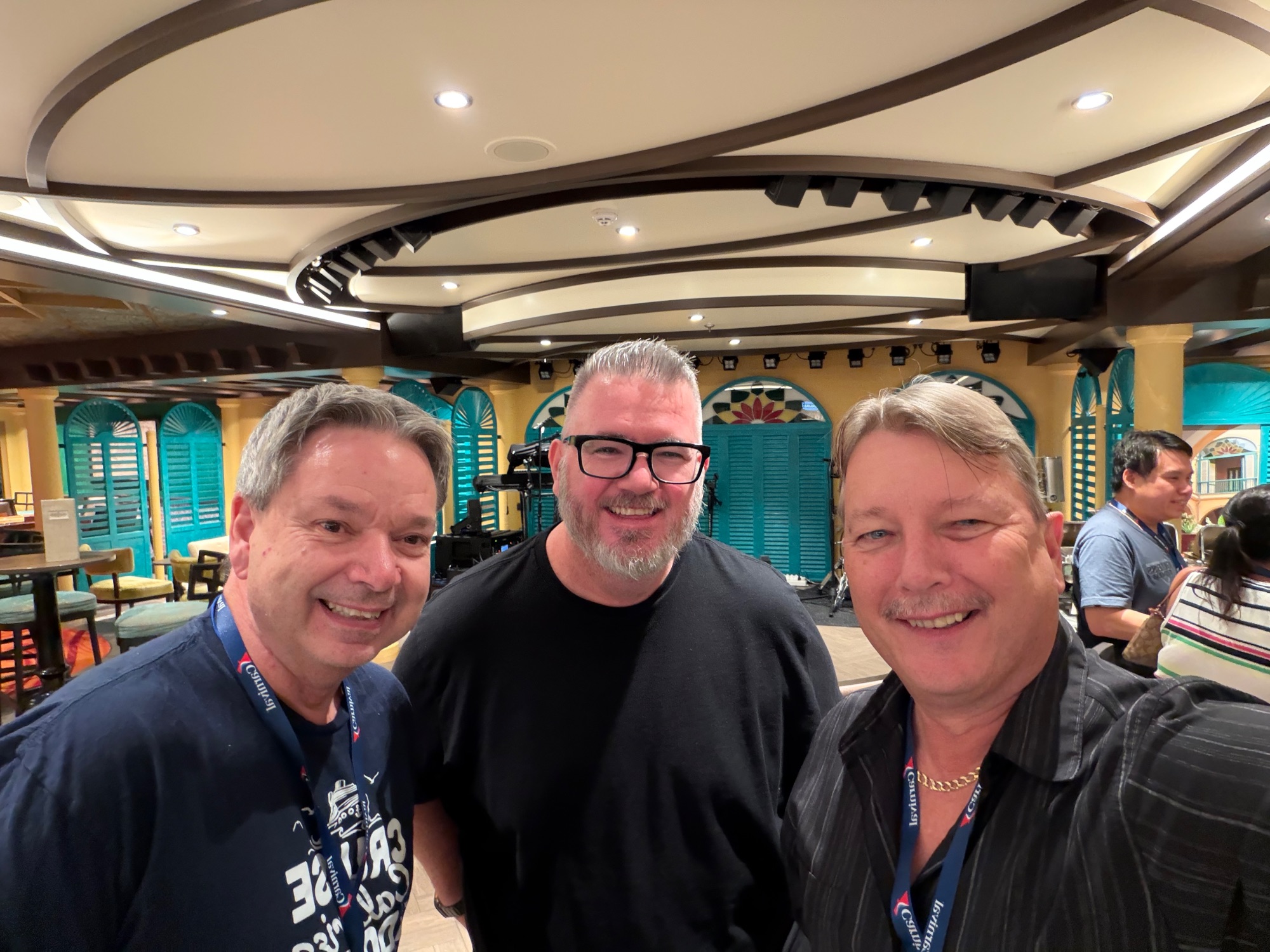 Three men smiling at camera inside a colorful ship dining venue with turquoise doors