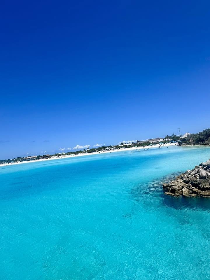 Turquoise shallow ocean water meeting white sand beach with resort buildings and palm trees along the shoreline