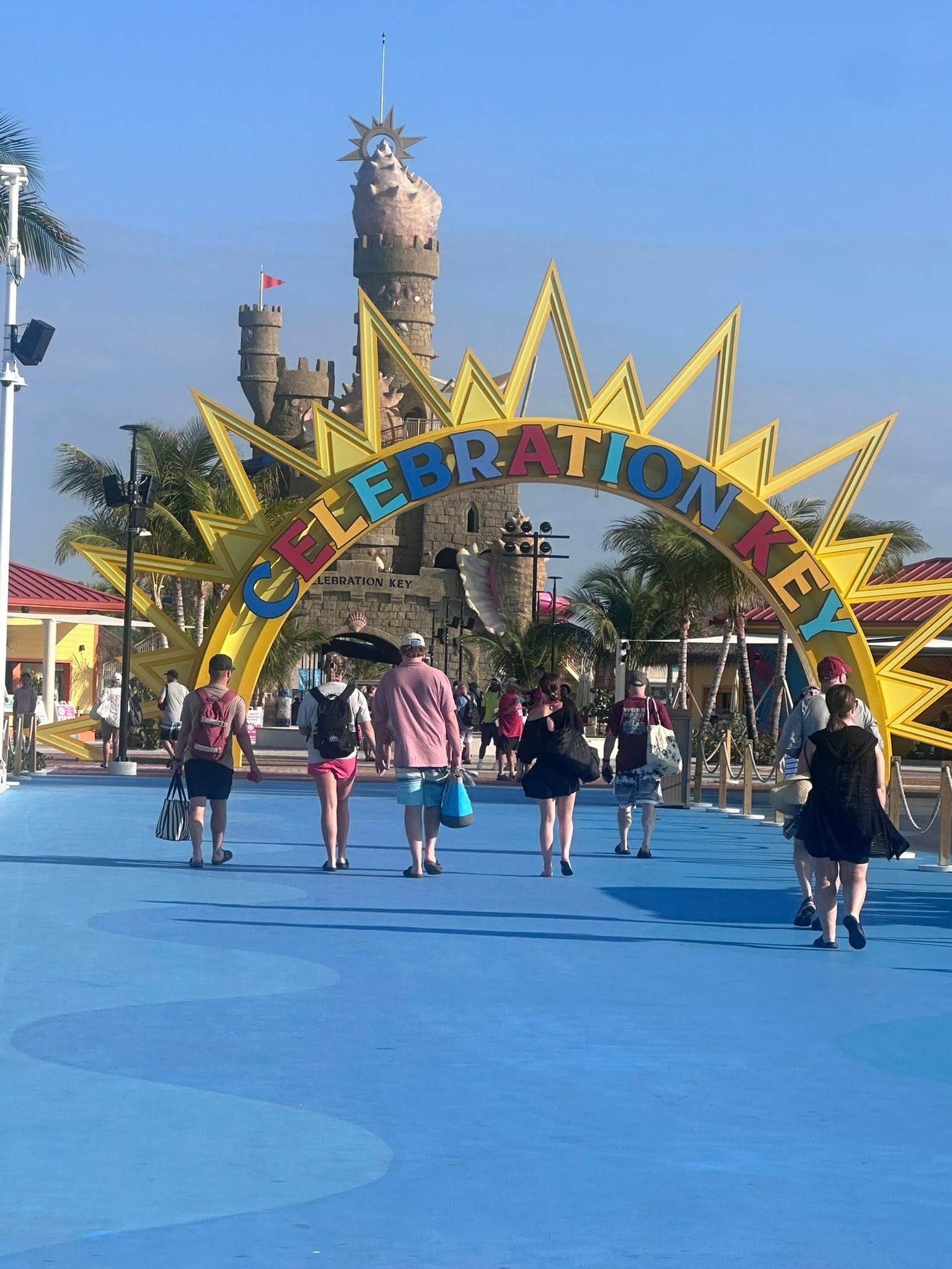Celebration Key entrance arch with yellow sun design, stone tower structure, and visitors on blue plaza in background