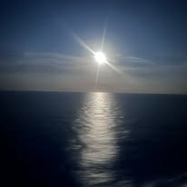 Bright sun reflecting on calm dark ocean water at dusk or dawn with clear sky above