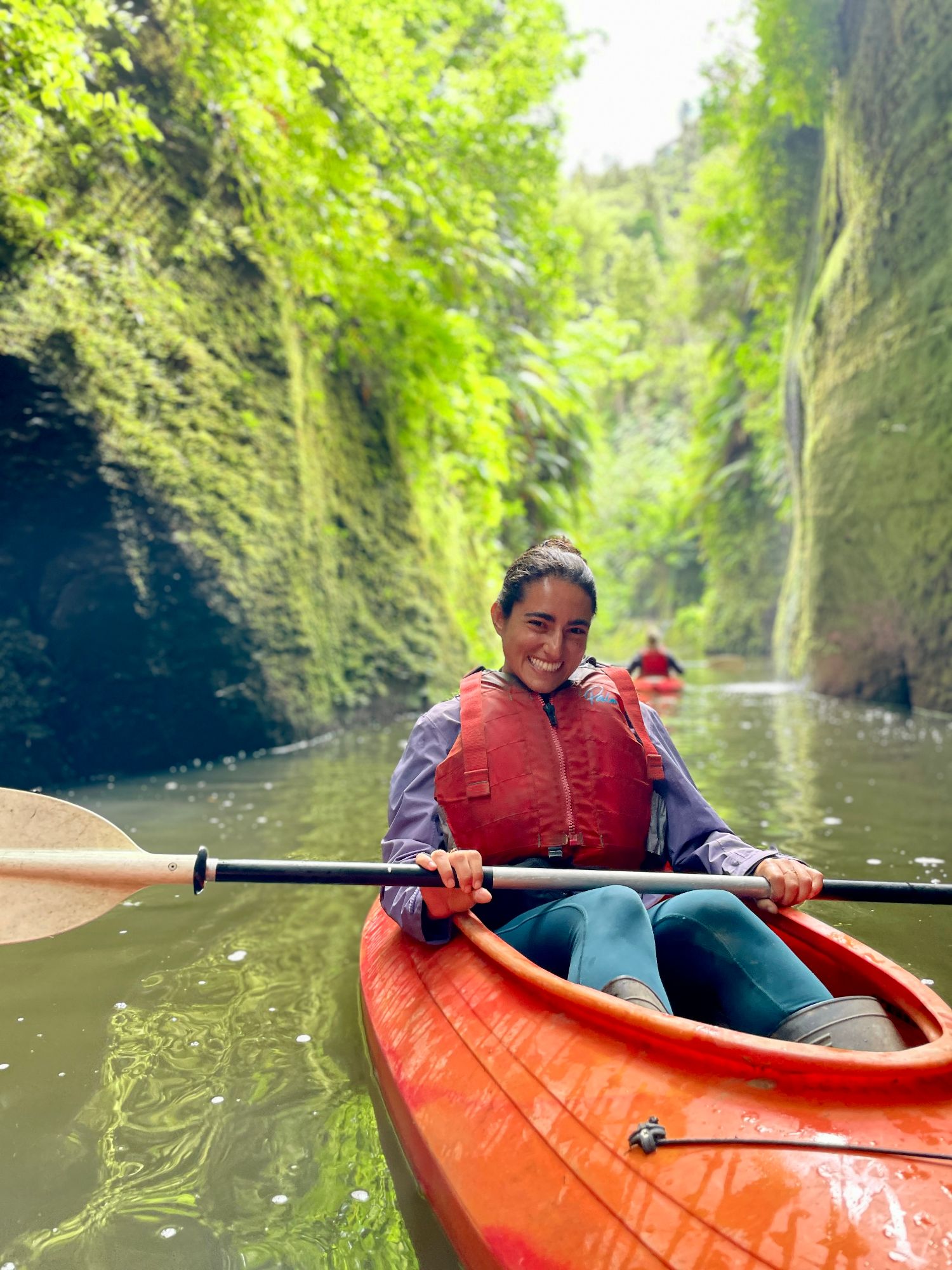 Julia kayaking through a narrow canyon with moss-covered rock walls towering on both sides of the water