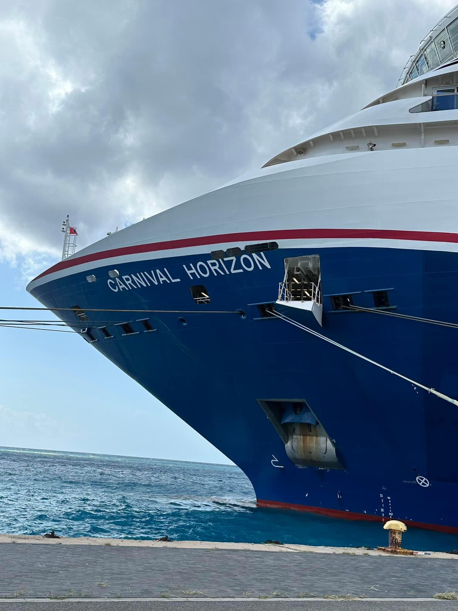 Close-up of the Carnival Horizon cruise ship's blue hull with red and white stripe docked at port