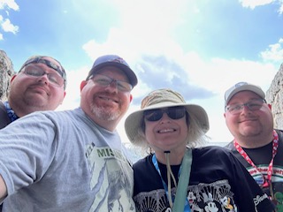 Four people posing together outdoors wearing casual vacation attire and lanyards at a Caribbean port