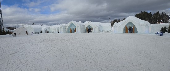 A row of white ice structures with arched doorways stands in a snowy landscape under cloudy skies