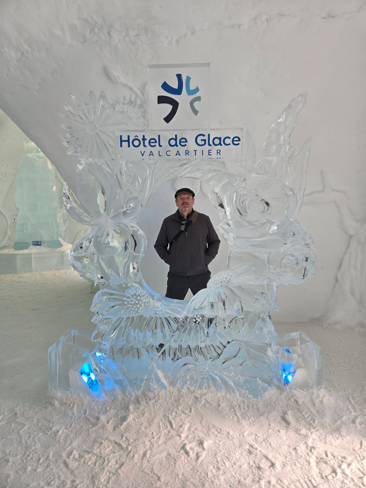 Daniel Coffin stands in front of an ice sculpture with the Hôtel de Glace Valcartier logo and blue-lit ice wings