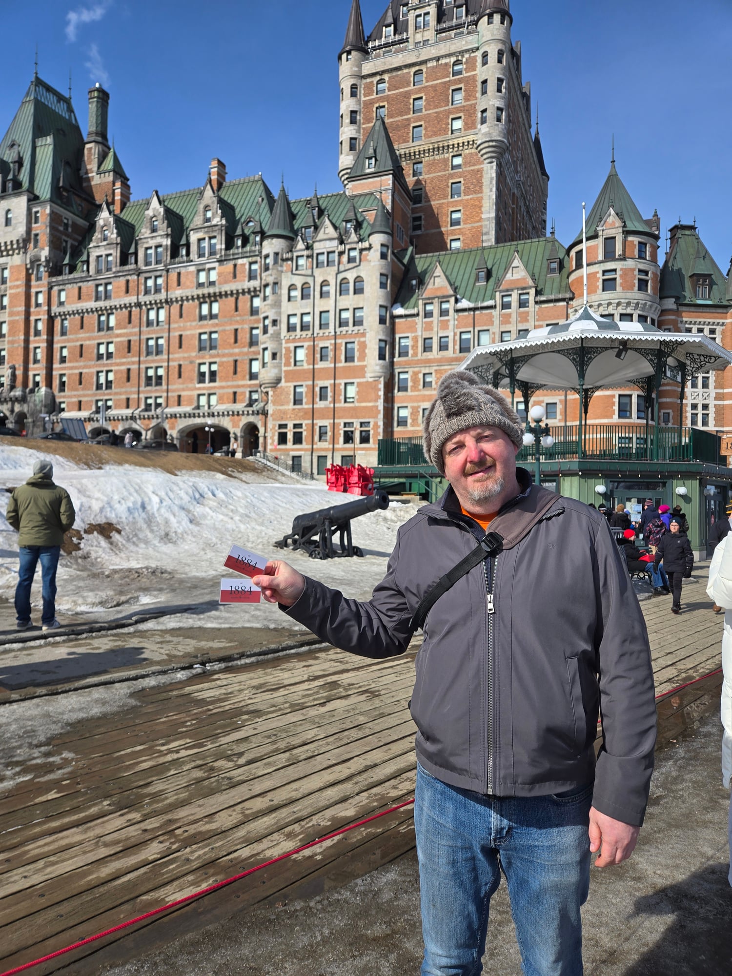 Daniel Coffin holds a 1884 marker on a wooden boardwalk with Château Frontenac and snow-covered landscape behind him in Quebec City