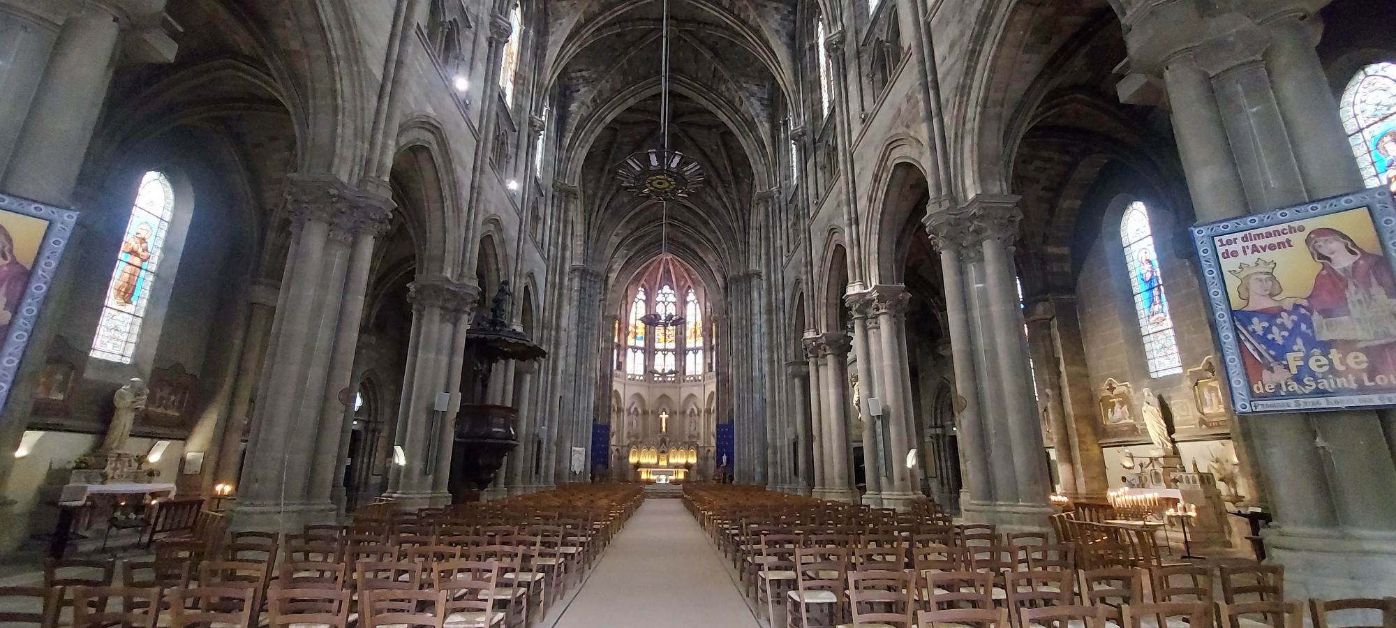 Interior of a Gothic cathedral with ribbed vaults, stained glass windows, and wooden pews