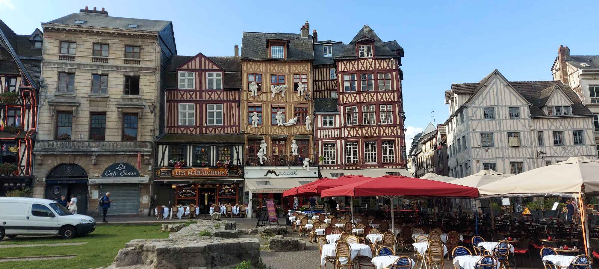 Half-timbered medieval buildings with red and cream facades lining a town square in Normandy