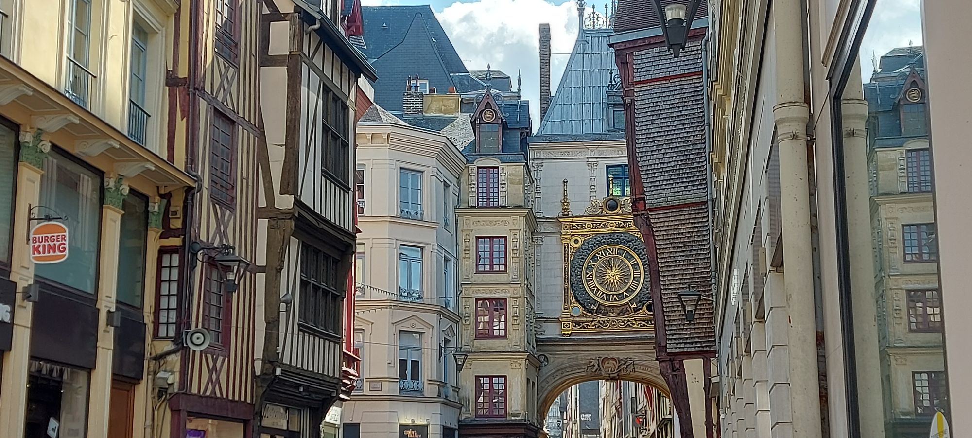 Narrow street between half-timbered buildings with a golden clock tower visible in the distance