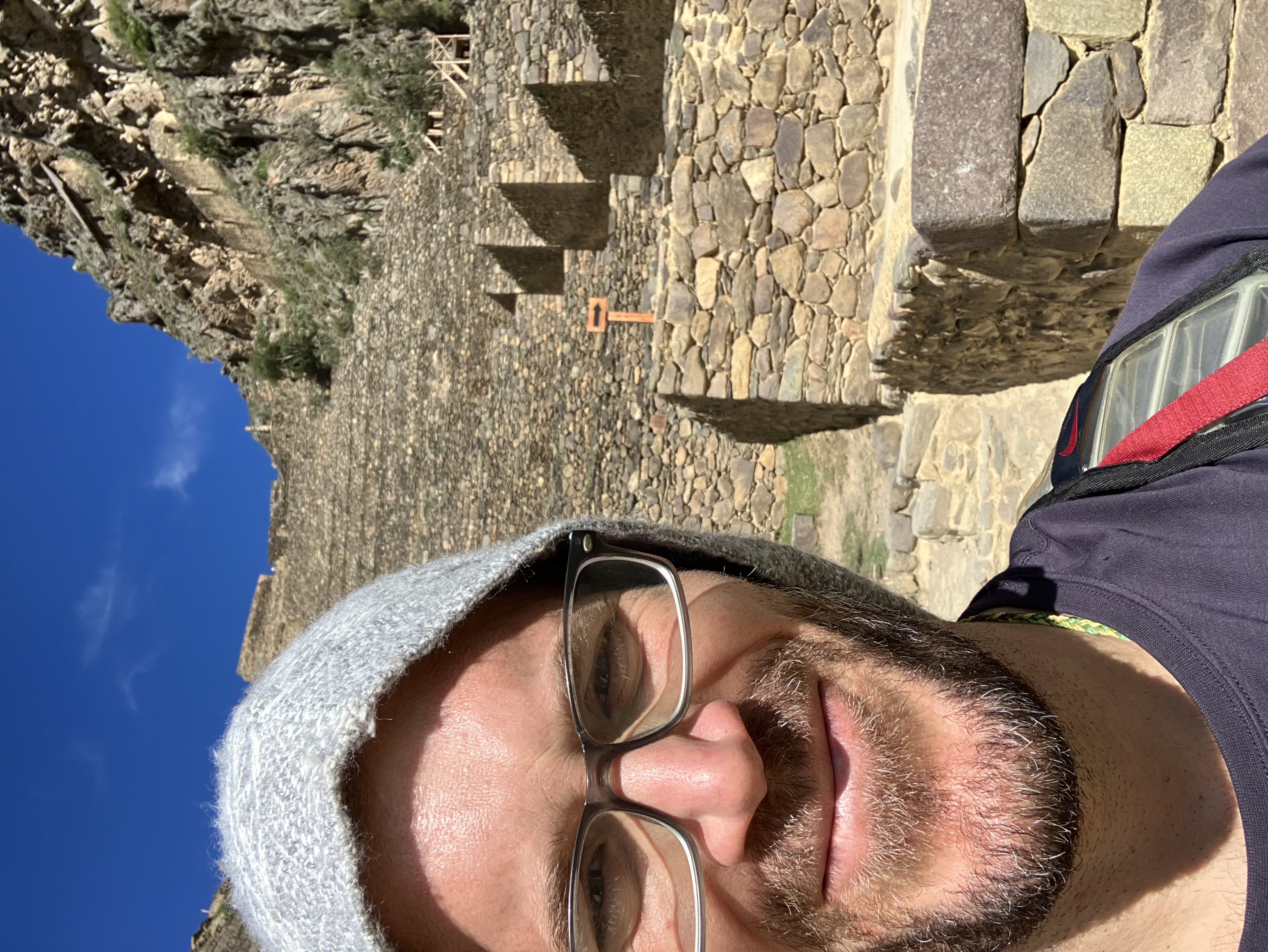Brian smiling at an Incan stone structure with fitted blocks and mountain terrain visible in the background