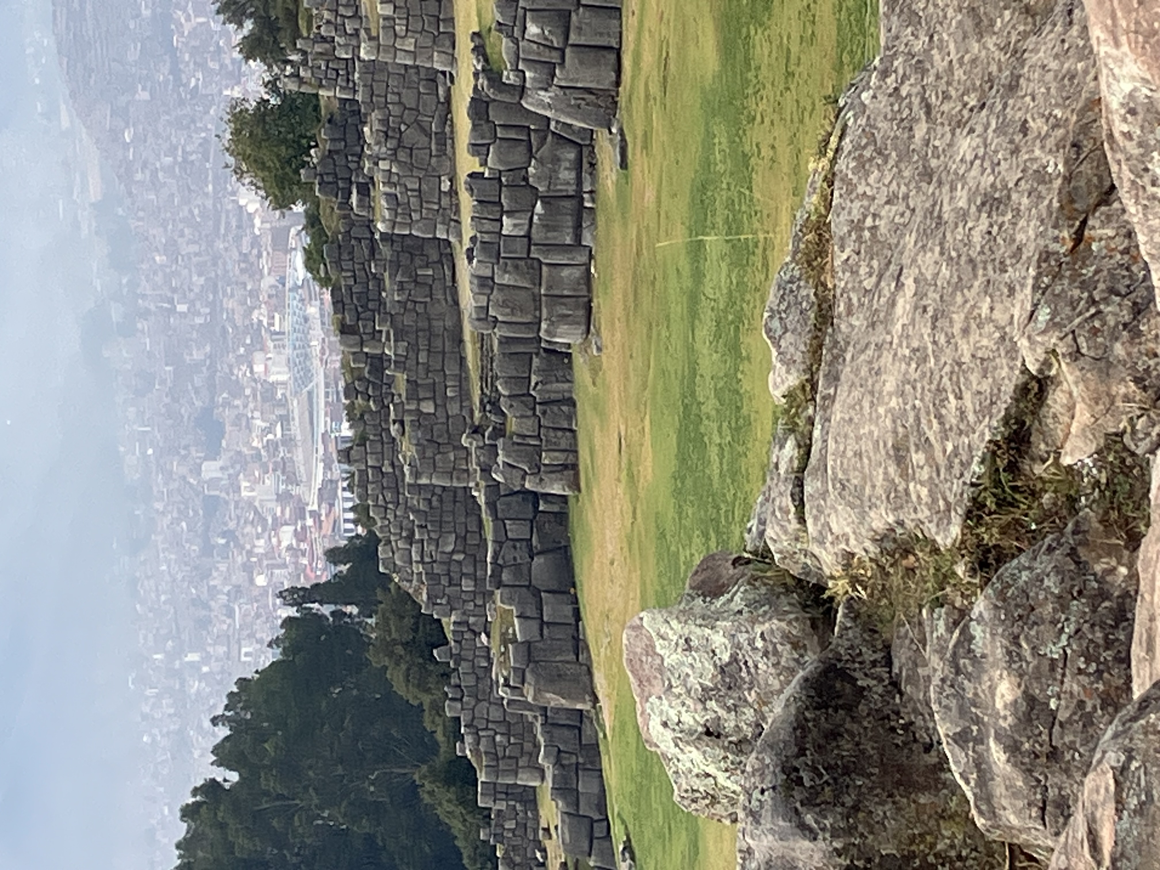 Incan stone ruins with massive fitted blocks overlooking a green valley and distant city nestled between mountains