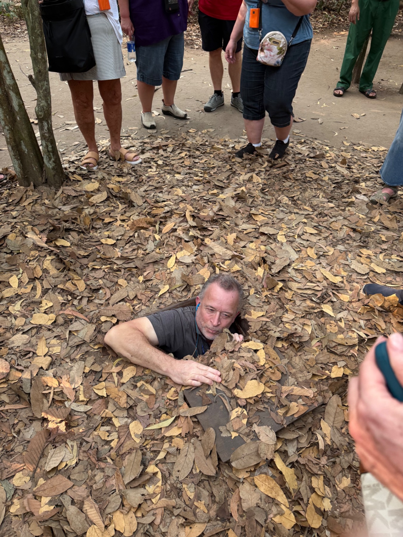 Man partially submerged in dried leaves surrounded by standing onlookers during a group activity