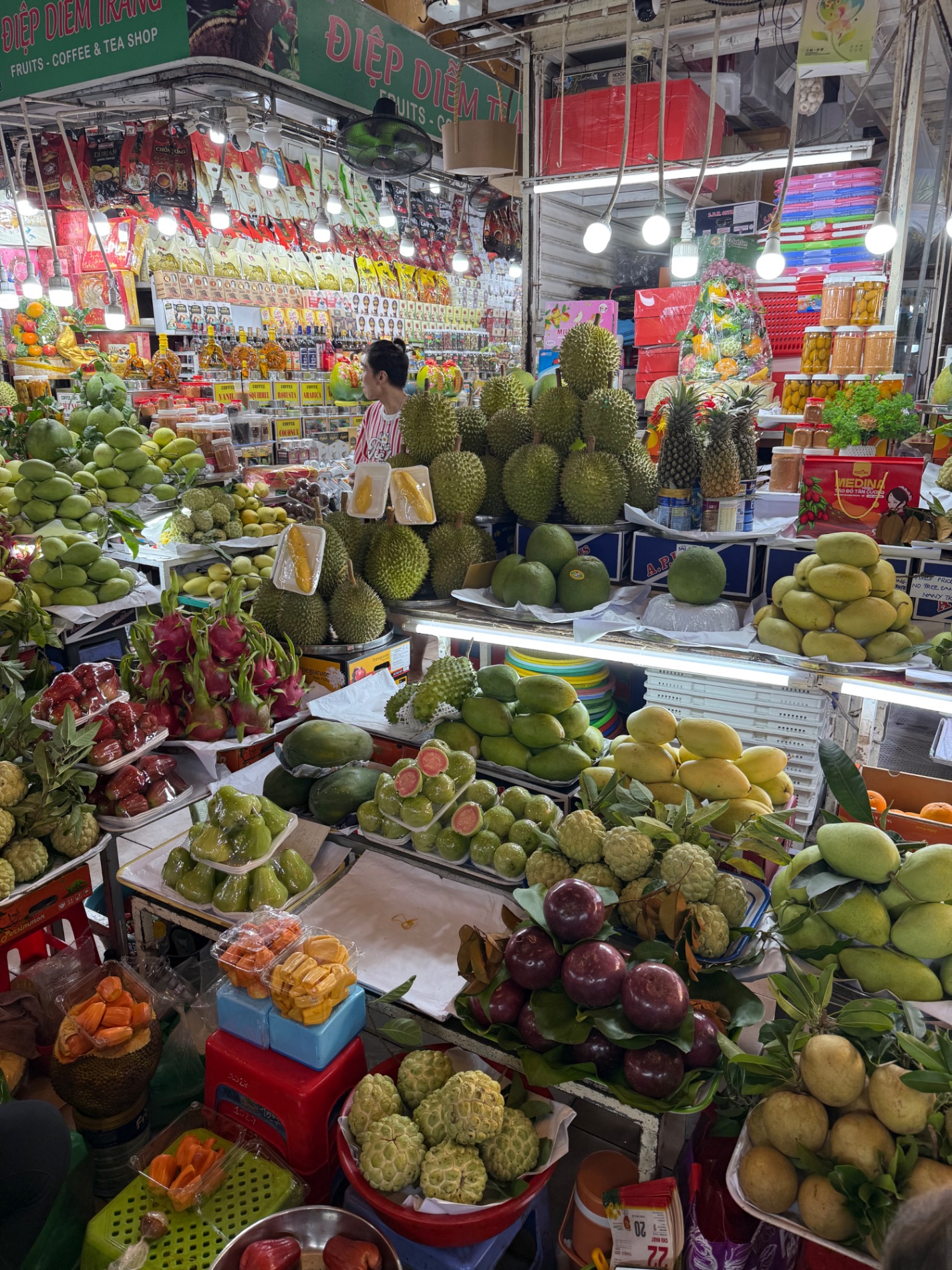 Colorful indoor fruit and vegetable market stall displaying durian, mangoes, dragon fruit and tropical produce