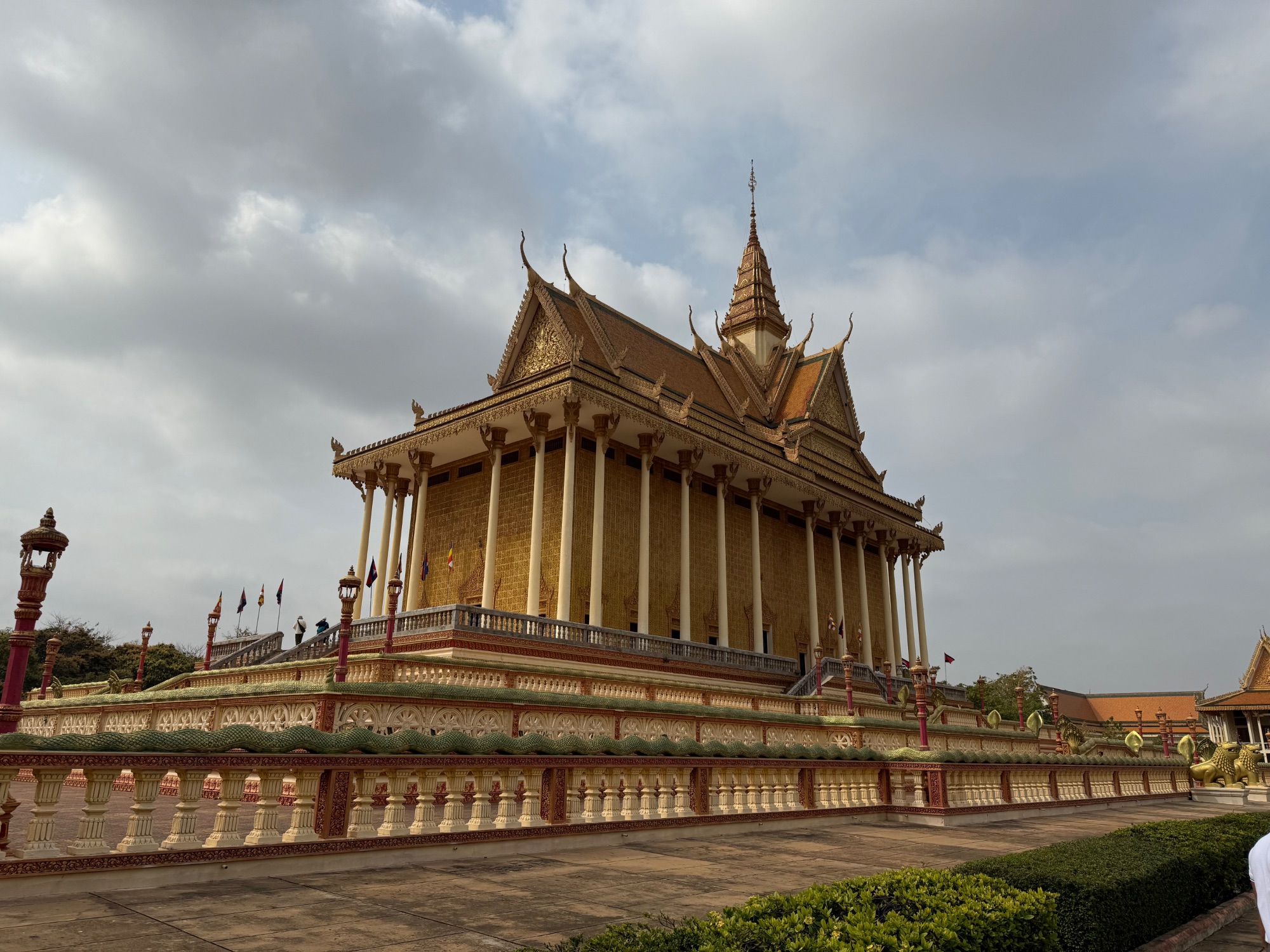 Golden-roofed Cambodian temple with ornate spires and white columns set against cloudy sky