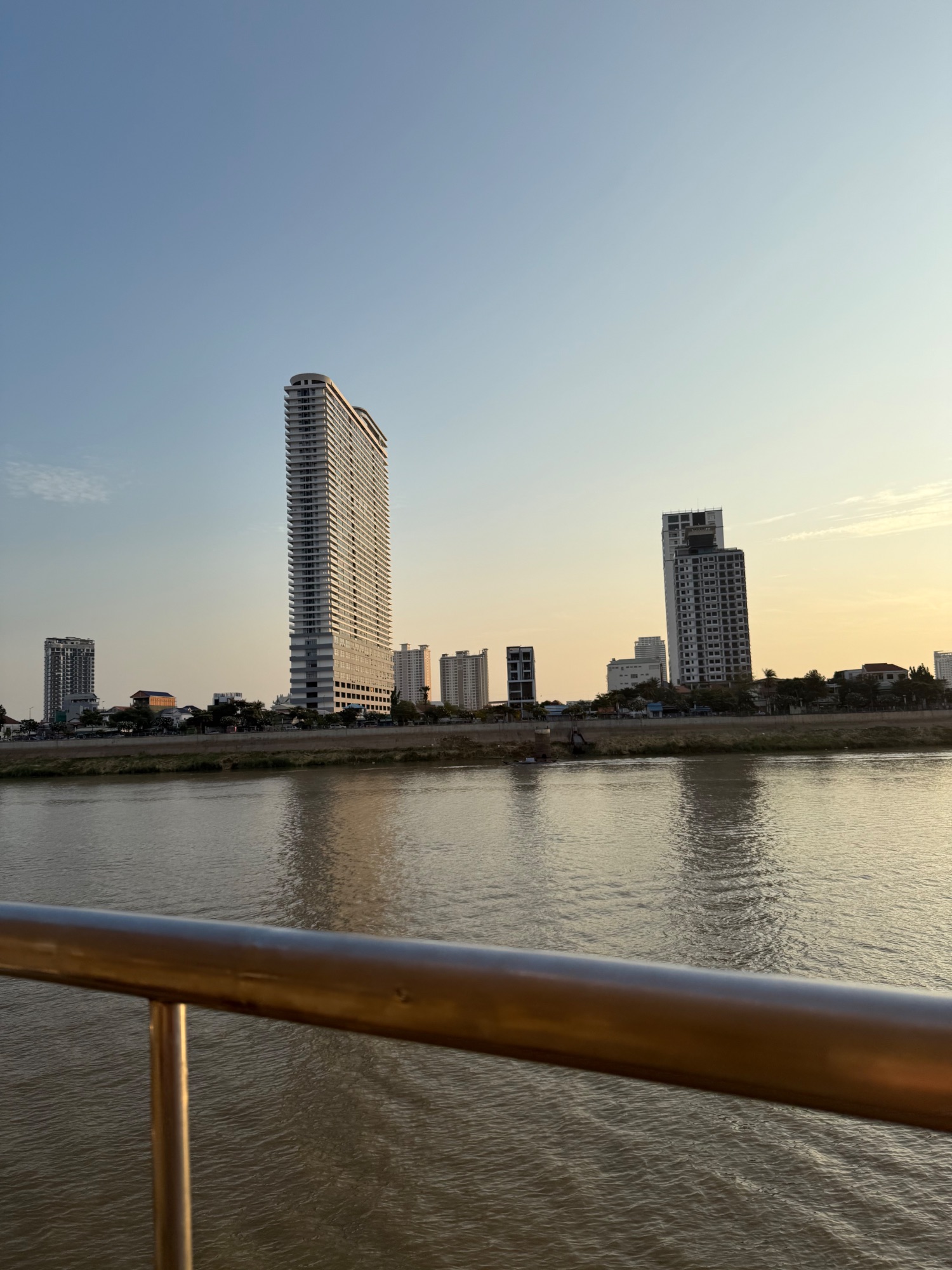 Modern high-rise residential buildings reflected in a wide river at dusk with grassy embankment