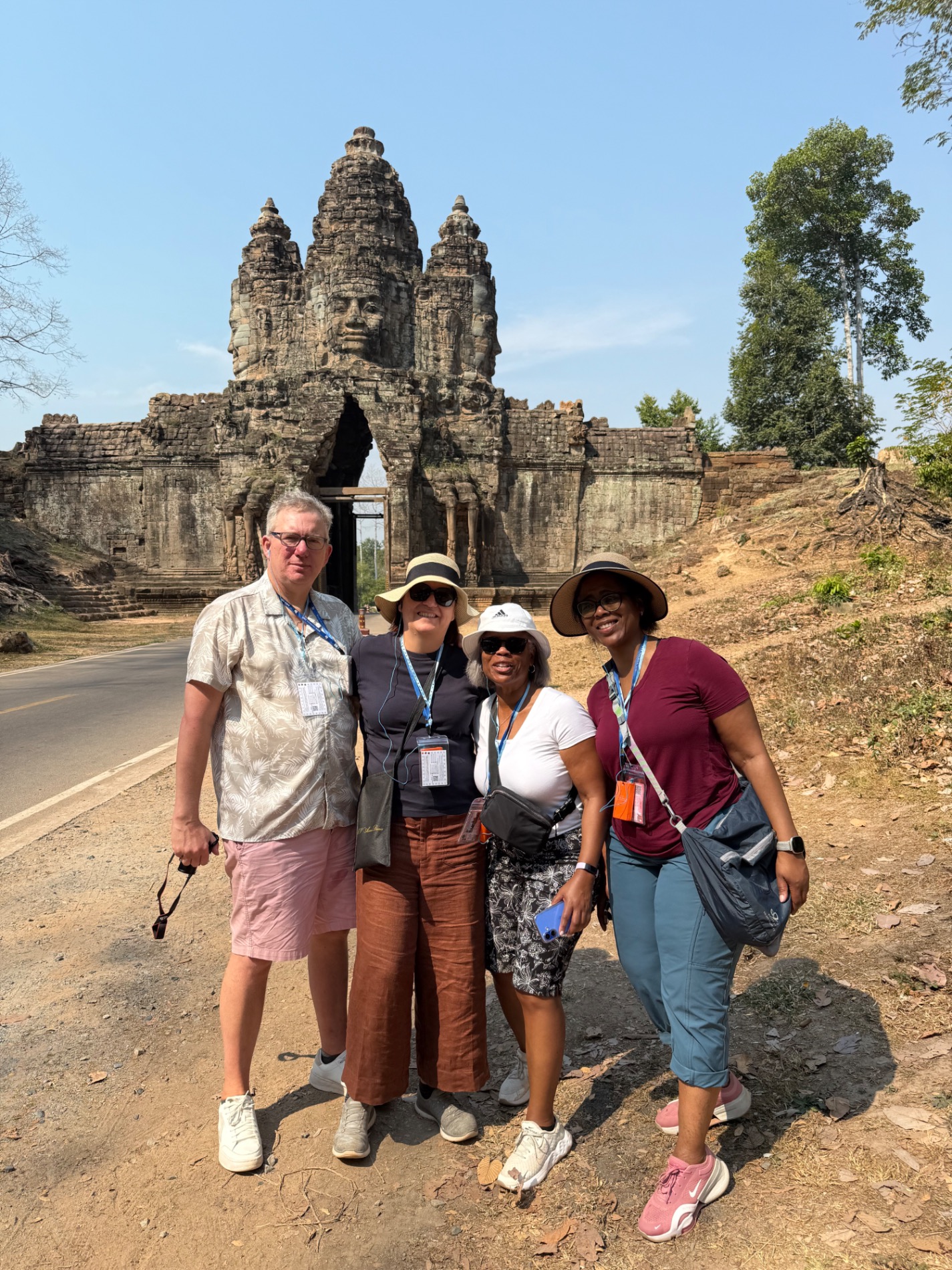 Four tourists posing together at stone gateway entrance to ancient Khmer temple ruins