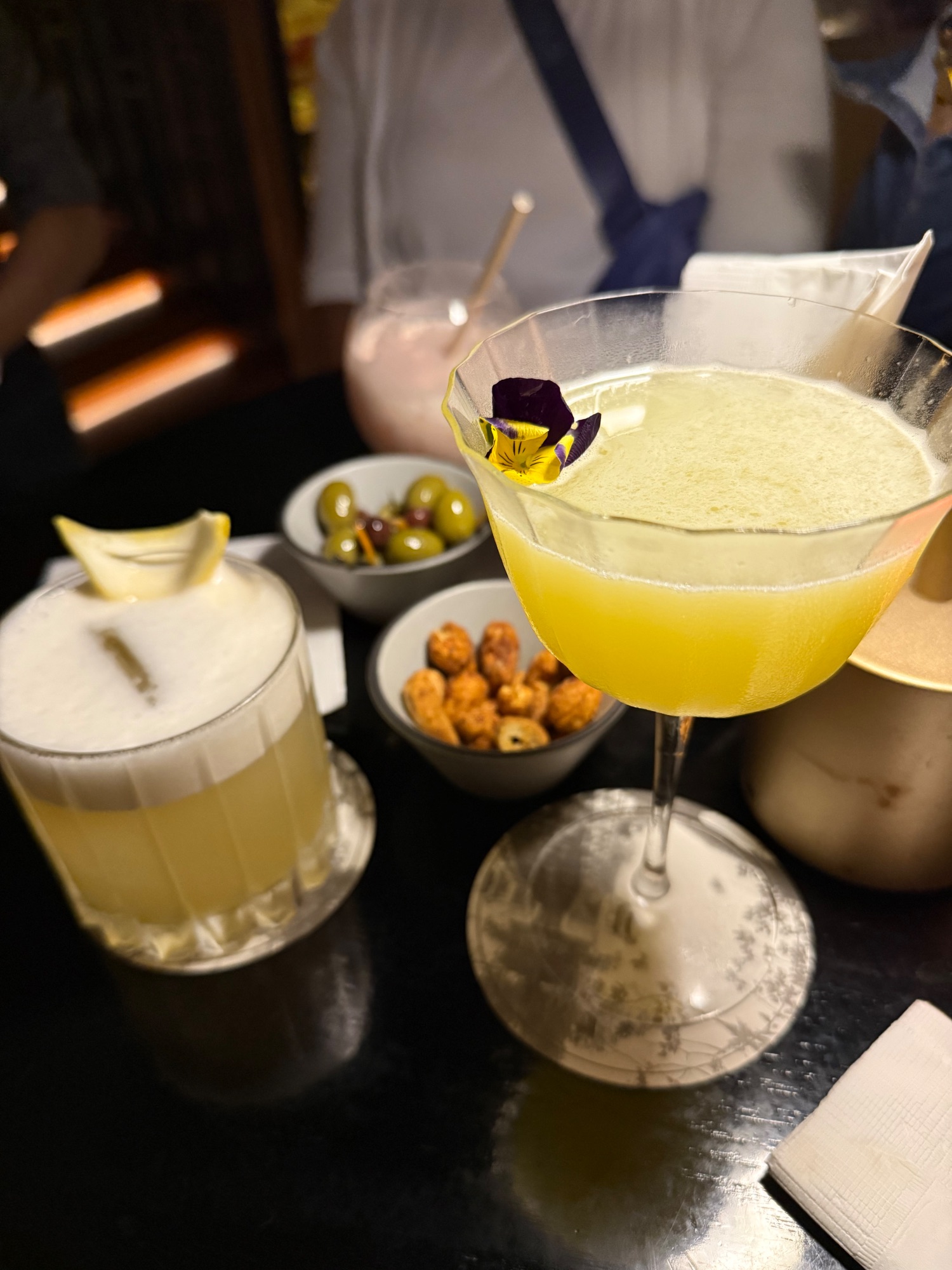 Cocktails with edible flowers and appetizers on dark table at upscale restaurant or bar