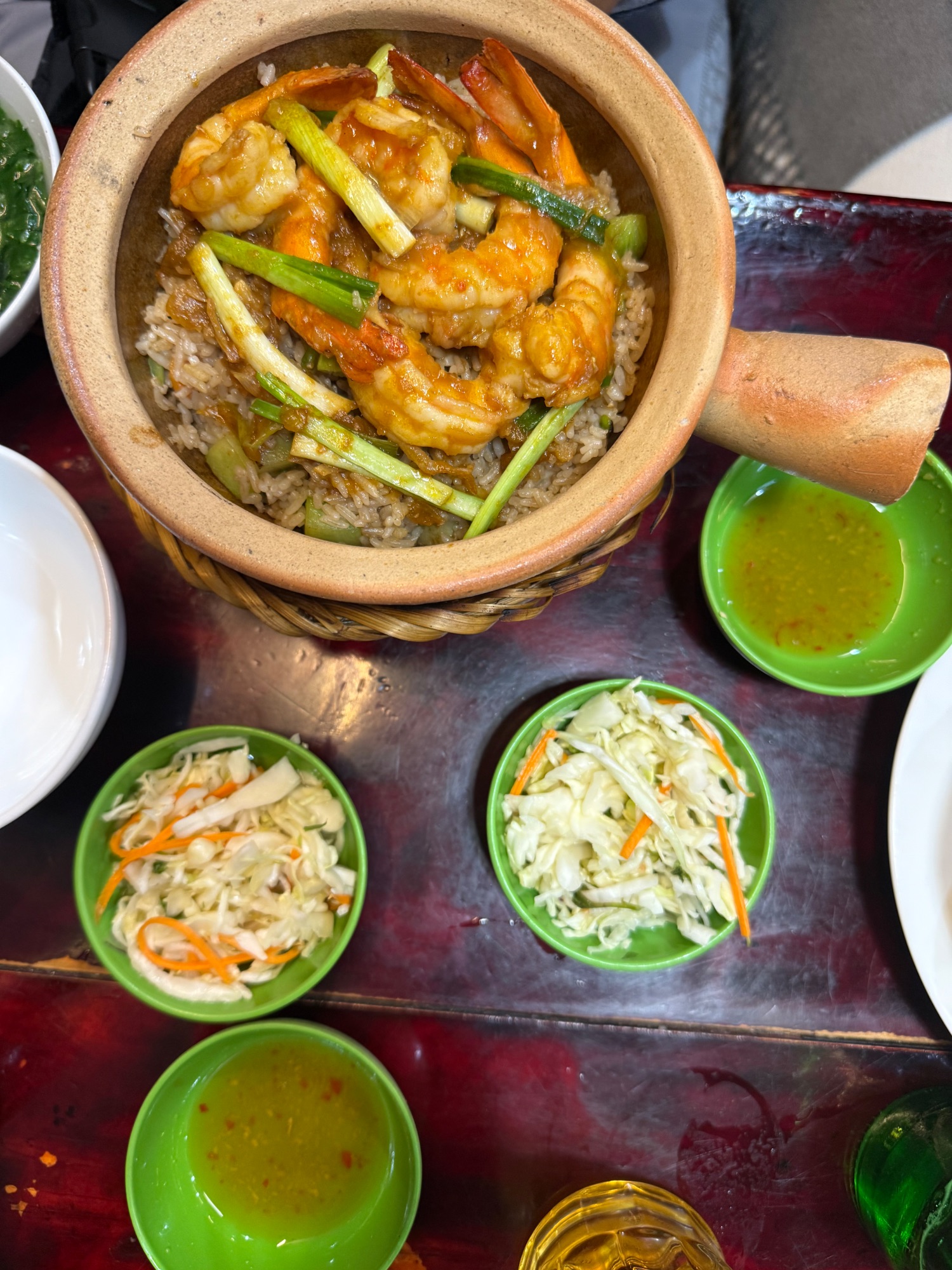 Clay pot of shrimp and rice with green vegetable sides and dipping sauce at Vietnamese restaurant