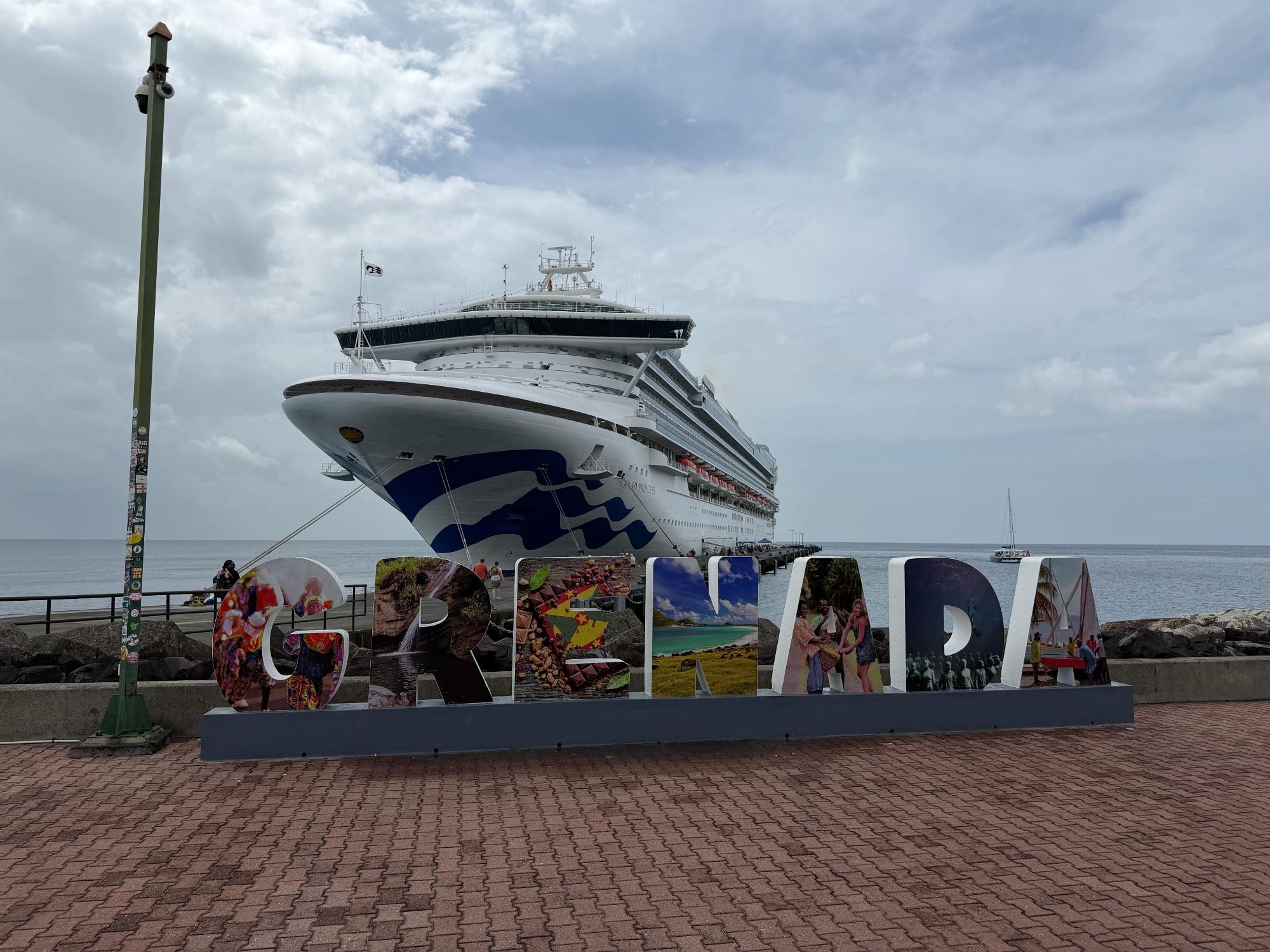 A bold GRENADA sign at the cruise port with a docked Princess Cruises ship looming behind it.