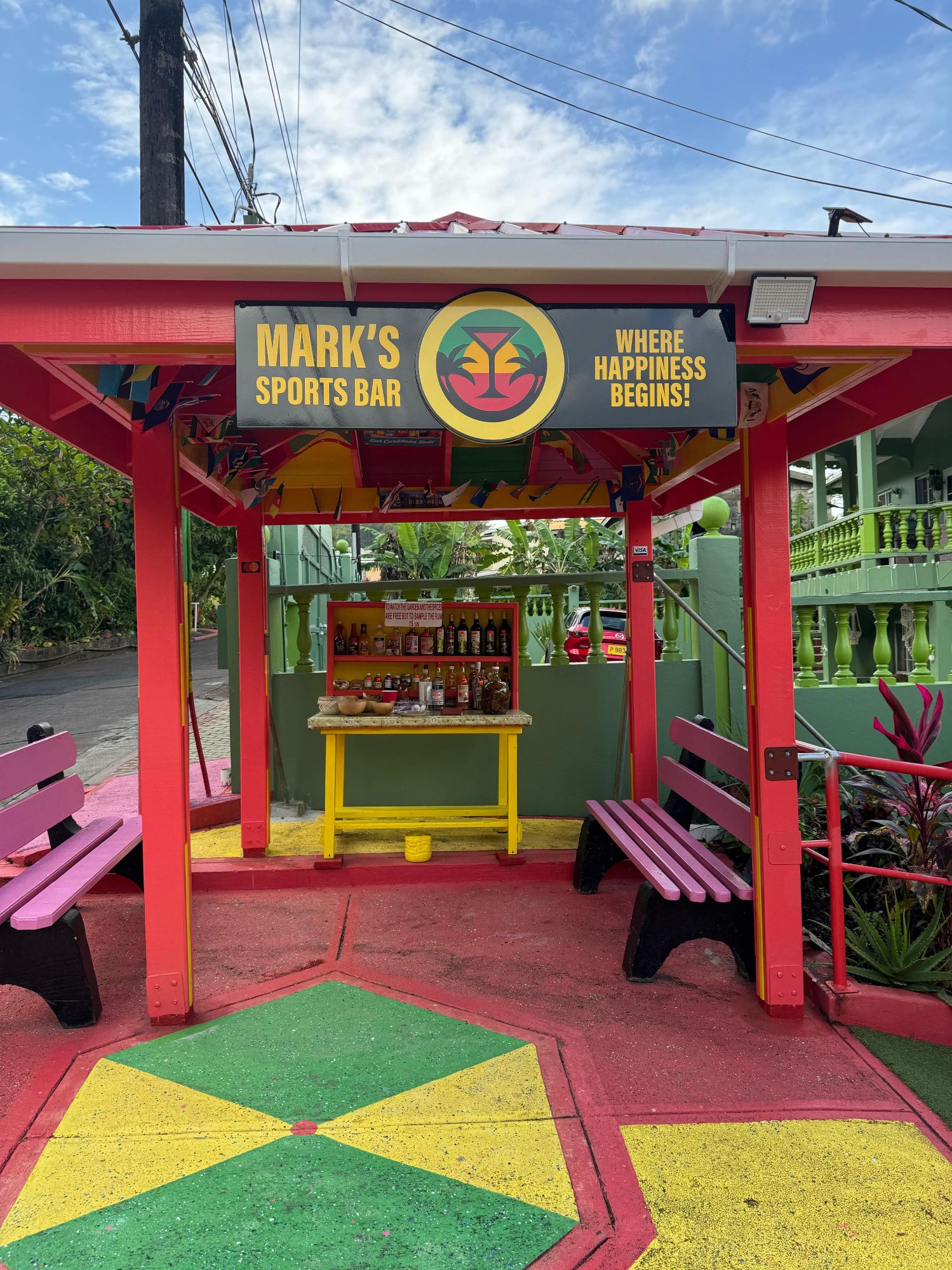 Mark's Sports Bar entrance adorned with vibrant Jamaican colors and a cheerful 'Where Happiness Begins' sign.