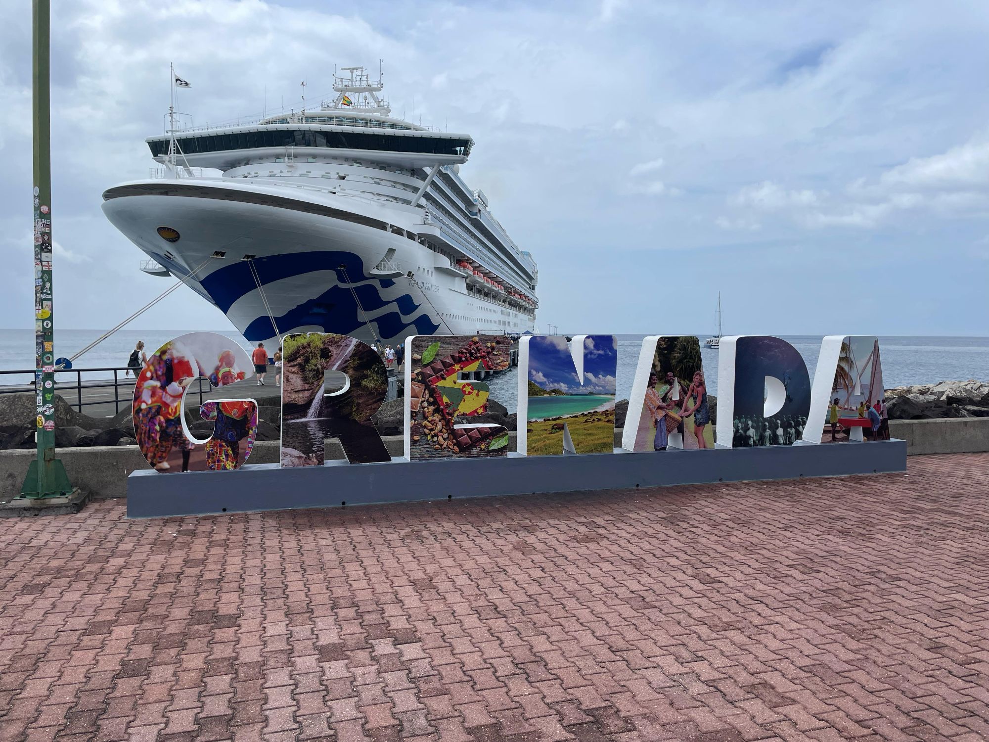 A colorful GRENADA sign stands at the cruise port with a massive Princess ship looming behind.