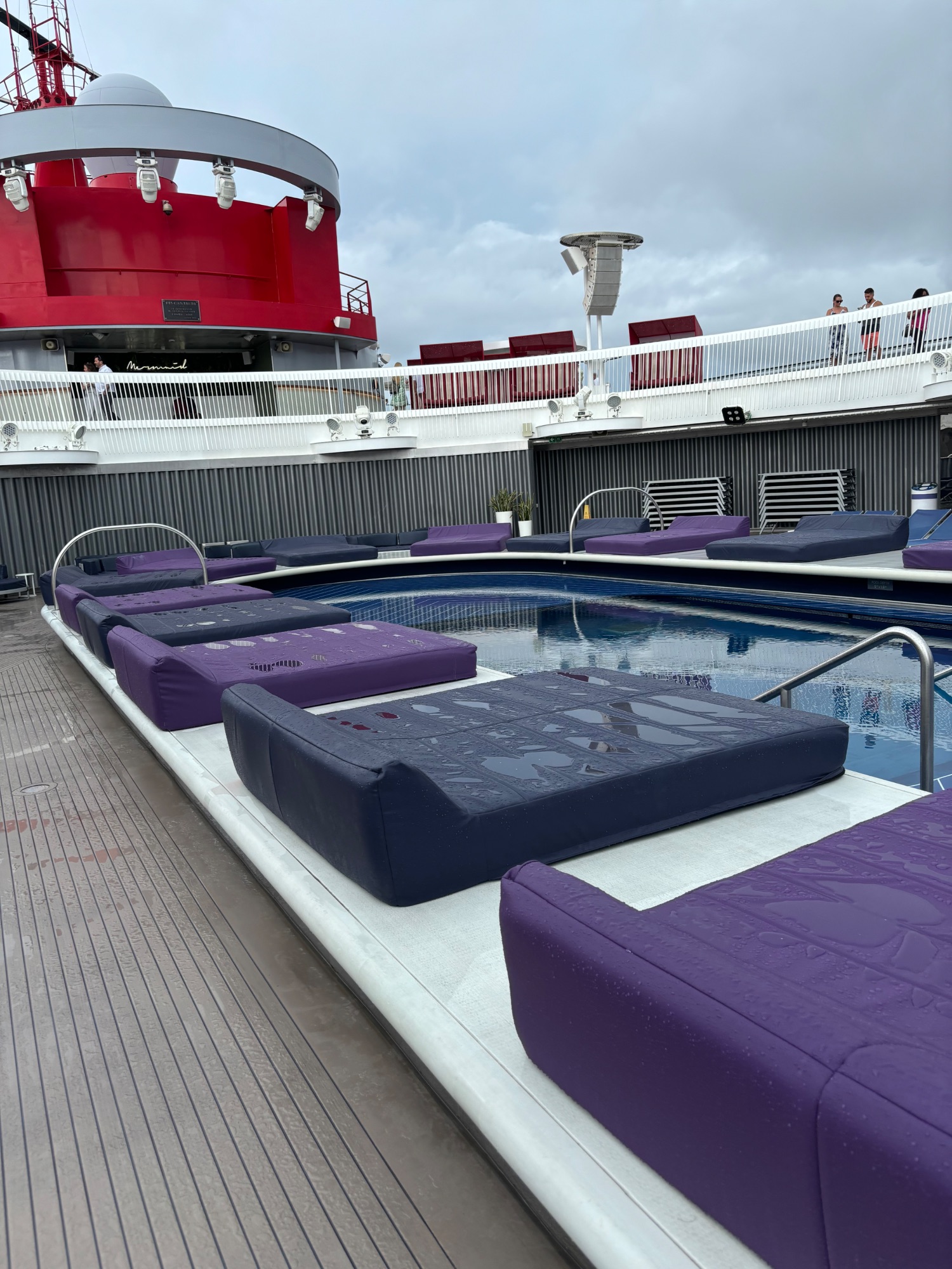 Swimming pool deck on a cruise ship with purple lounge chairs and a red funnel visible
