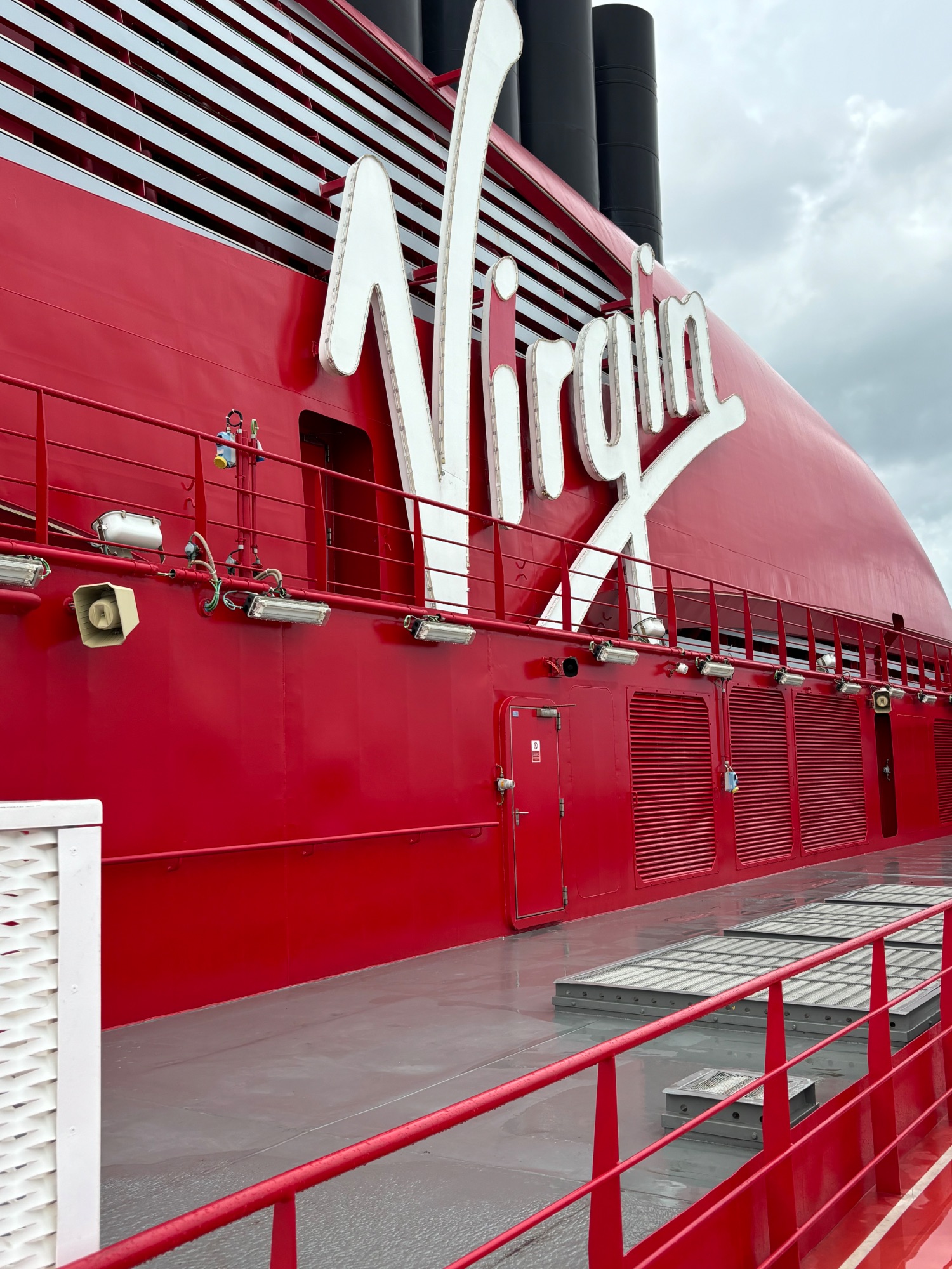 Red VIRGIN text on the side of a cruise ship hull with white railings