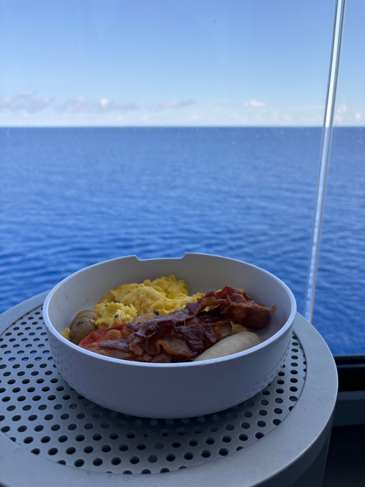 Breakfast bowl with eggs, bacon and potatoes on a ship railing overlooking open ocean