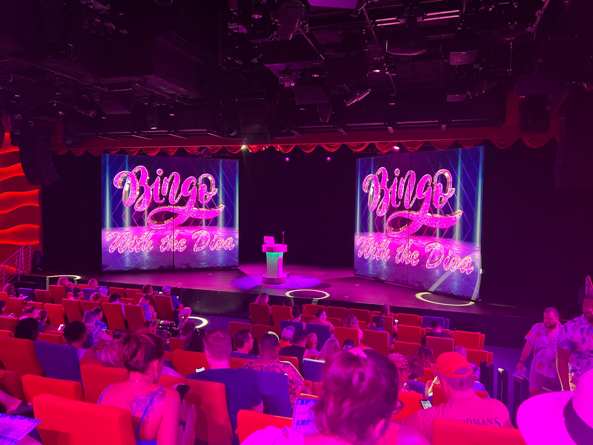 Theater interior with red seats and pink neon Bingo With the Diva signage on stage