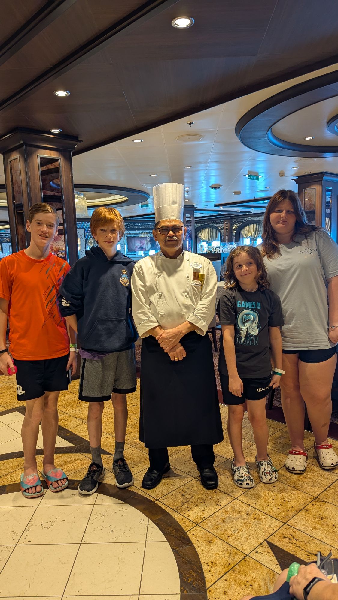 Family of five posing with chef in white uniform in dining area aboard Anthem of the Seas