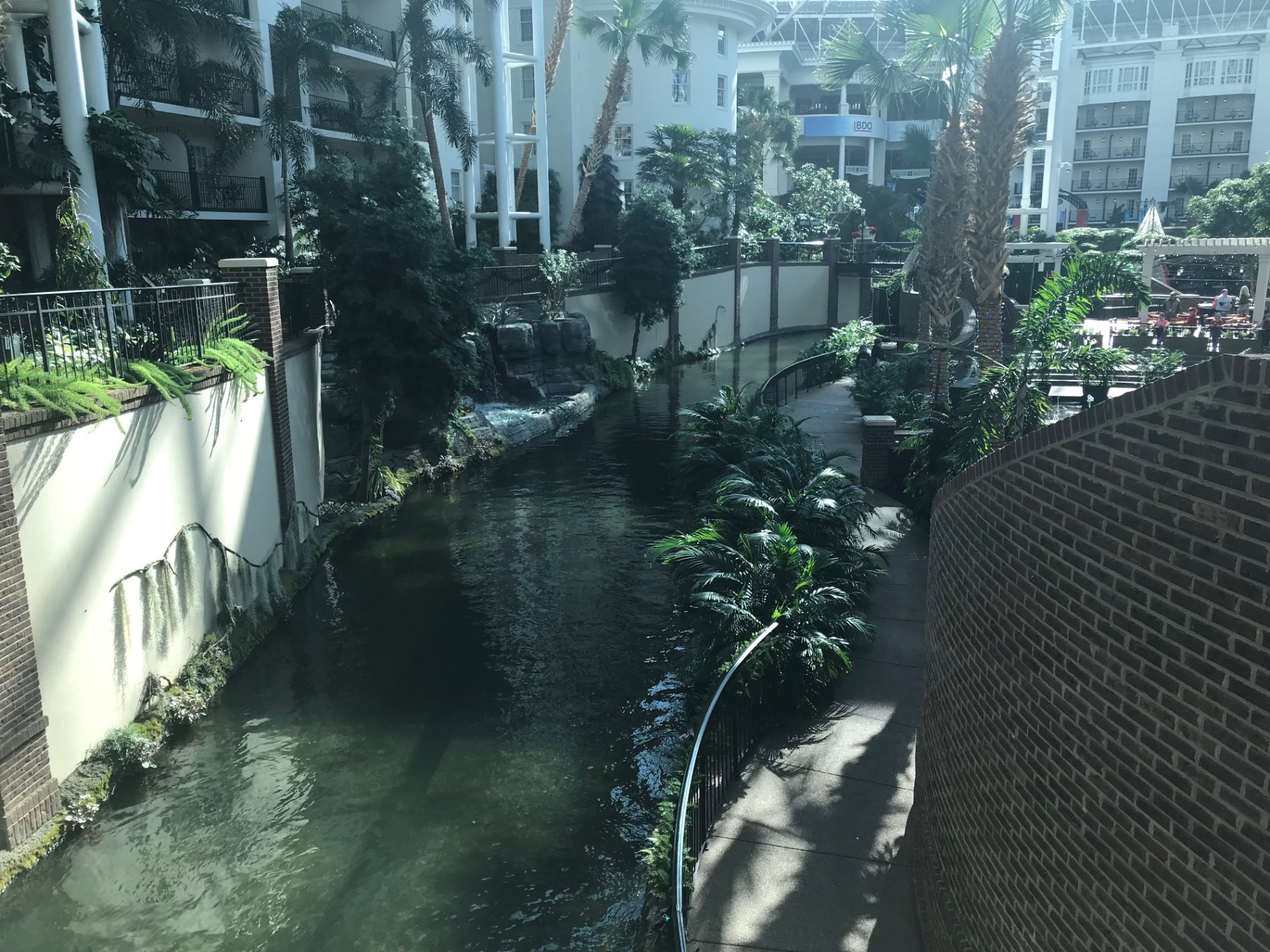 Narrow waterway between modern white buildings with palm trees and brick walls, showing calm water and pedestrian bridges
