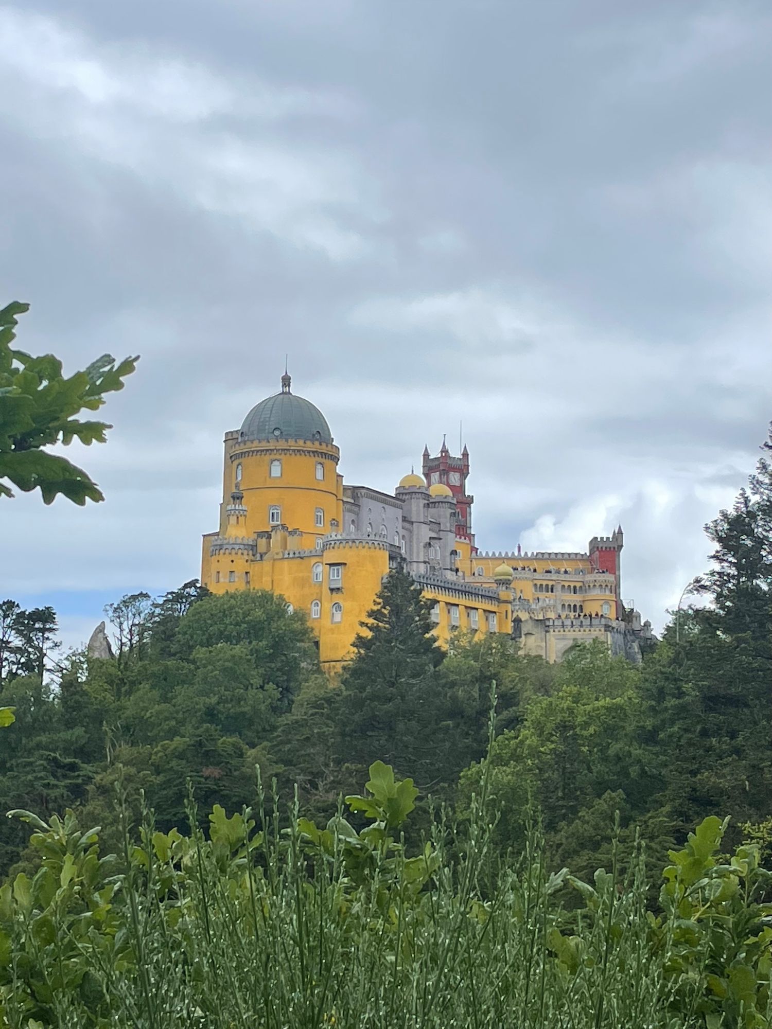 Bright yellow Pena Palace perched on a hilltop surrounded by lush green forest under cloudy skies