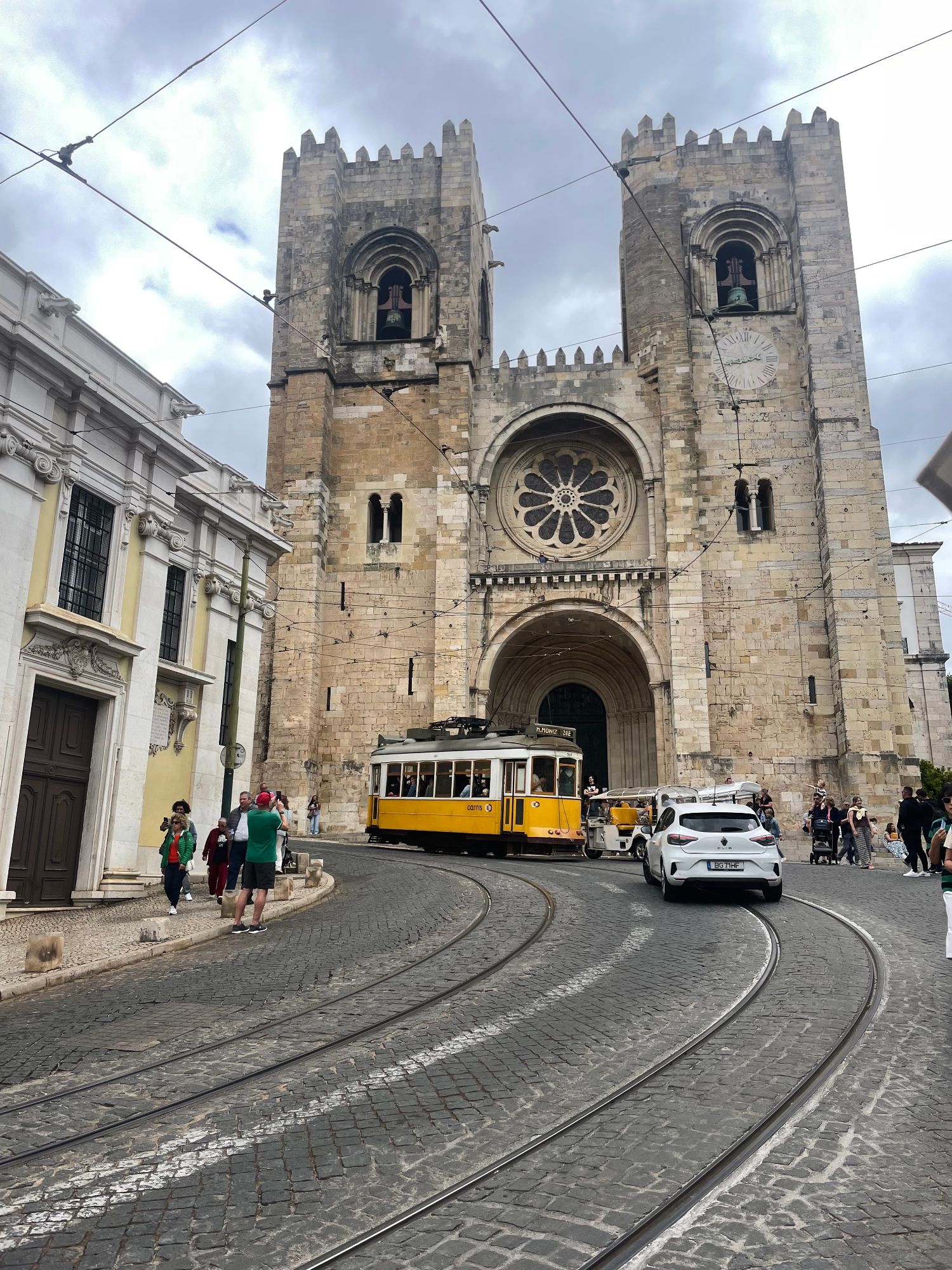 Yellow tram passing the historic Cathedral in Lisbon with twin stone towers and rose window