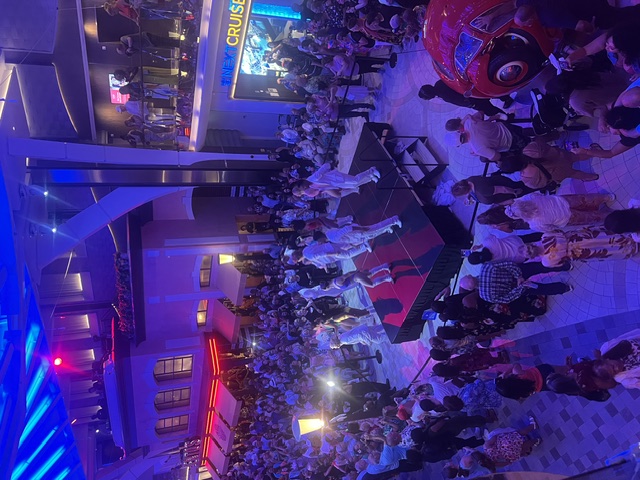 Crowded indoor venue with blue and purple lighting, people dancing on a central stage platform