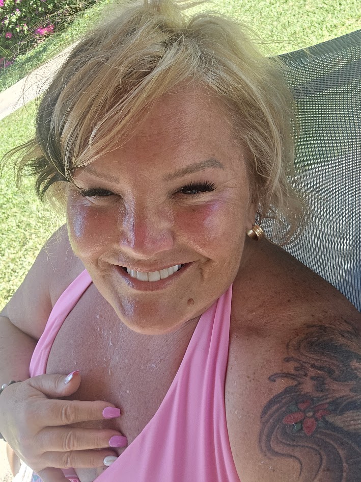 Joni Davis smiling at camera wearing pink bikini top poolside in bright sunlight